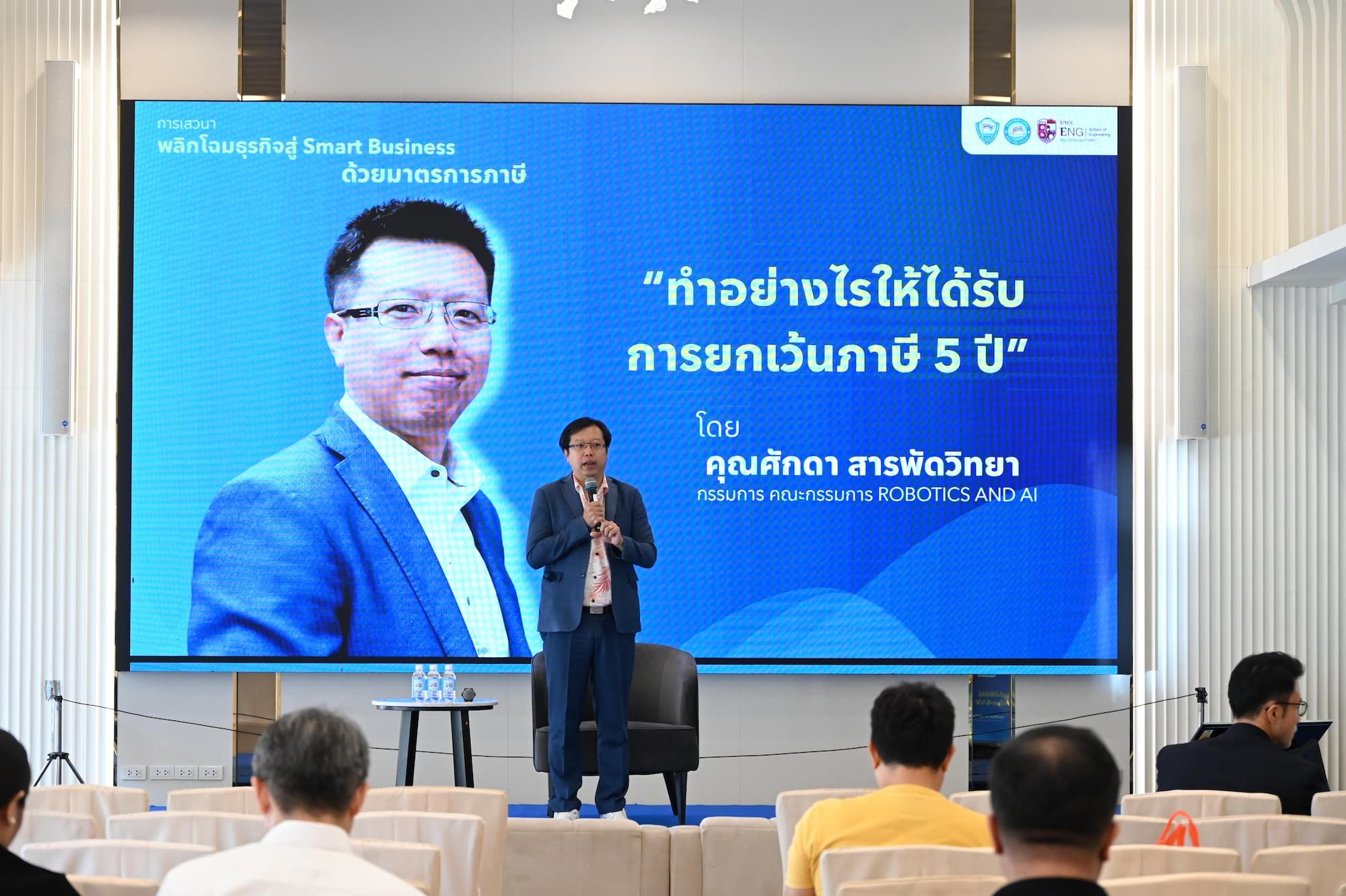 Man speaking on stage in front of a screen displaying 'How to get a 5-year tax exemption'.