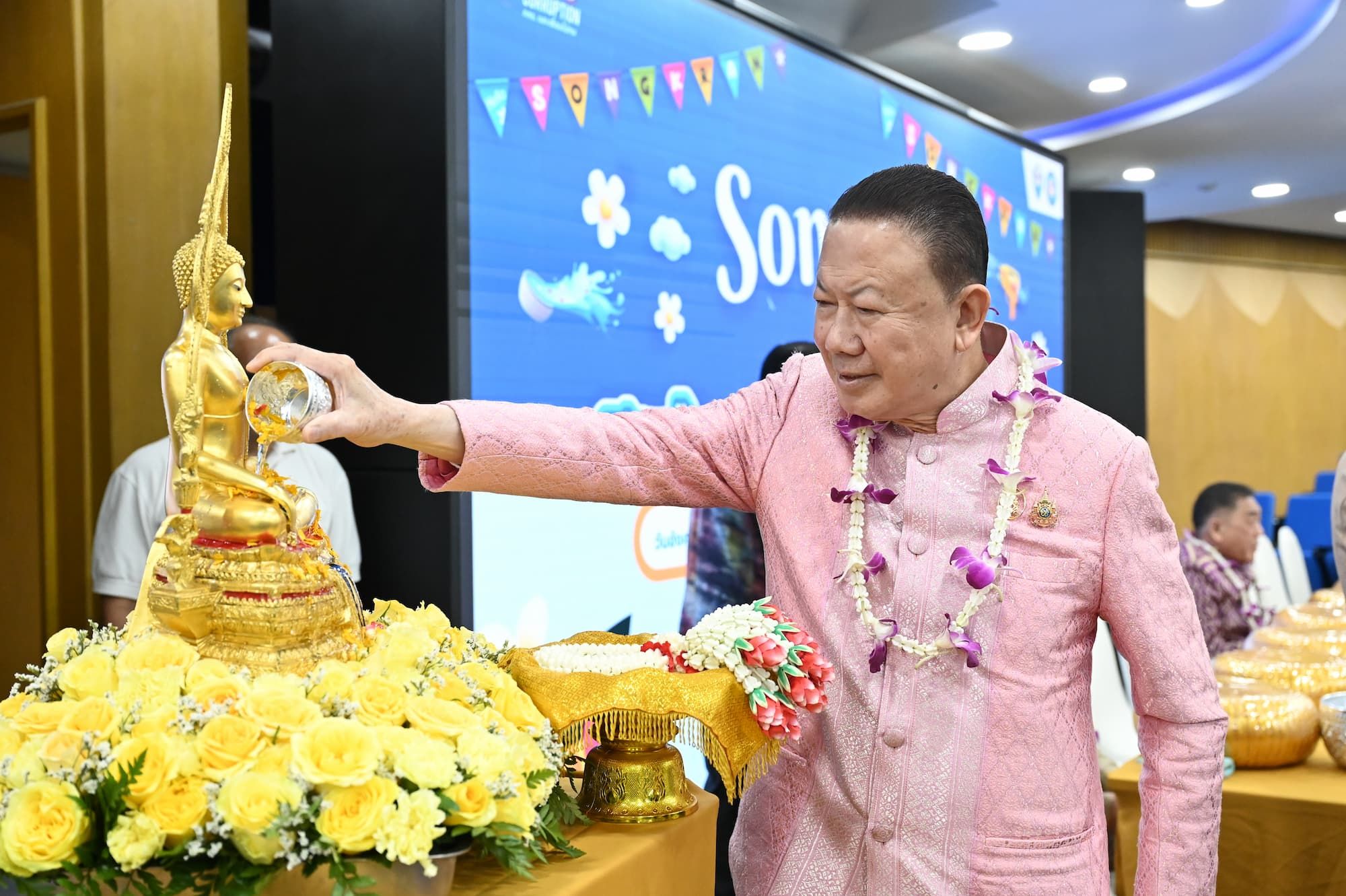 Man in pink pours water over a golden Buddha statue adorned with yellow flowers, celebrating Songkran.
