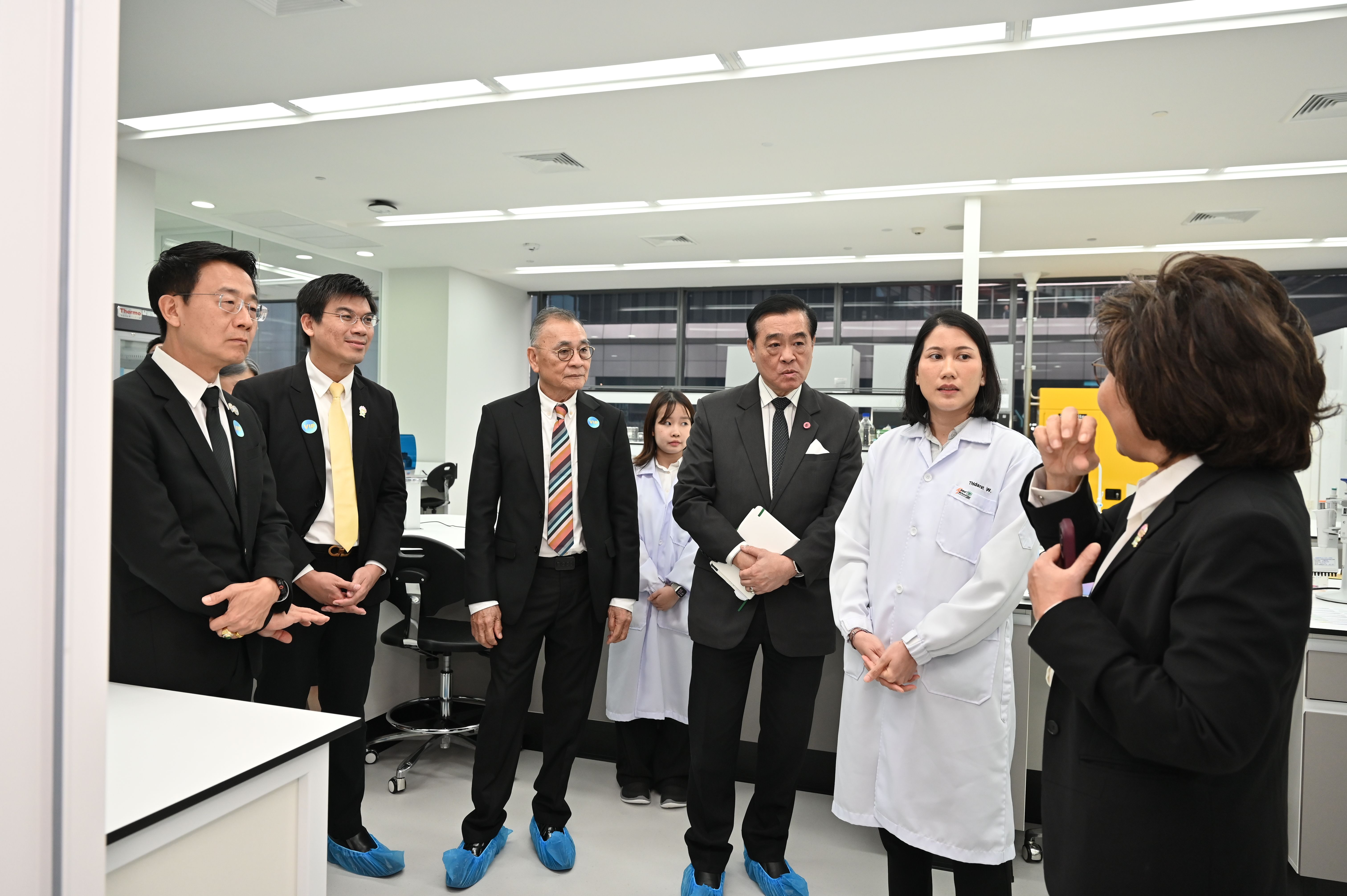 Professionals and scientists in a lab discussing research, wearing blue shoe covers.