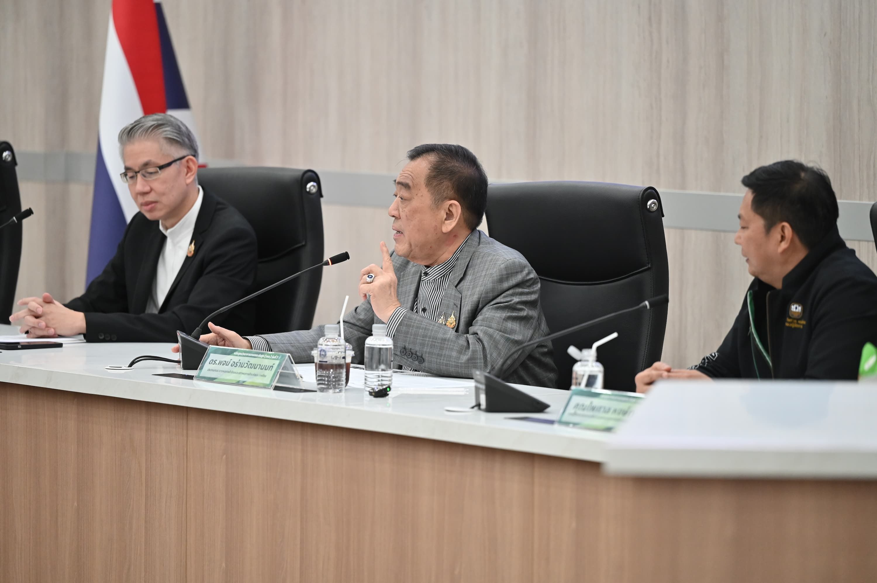 Three men in business attire seated at a conference table, one speaking.