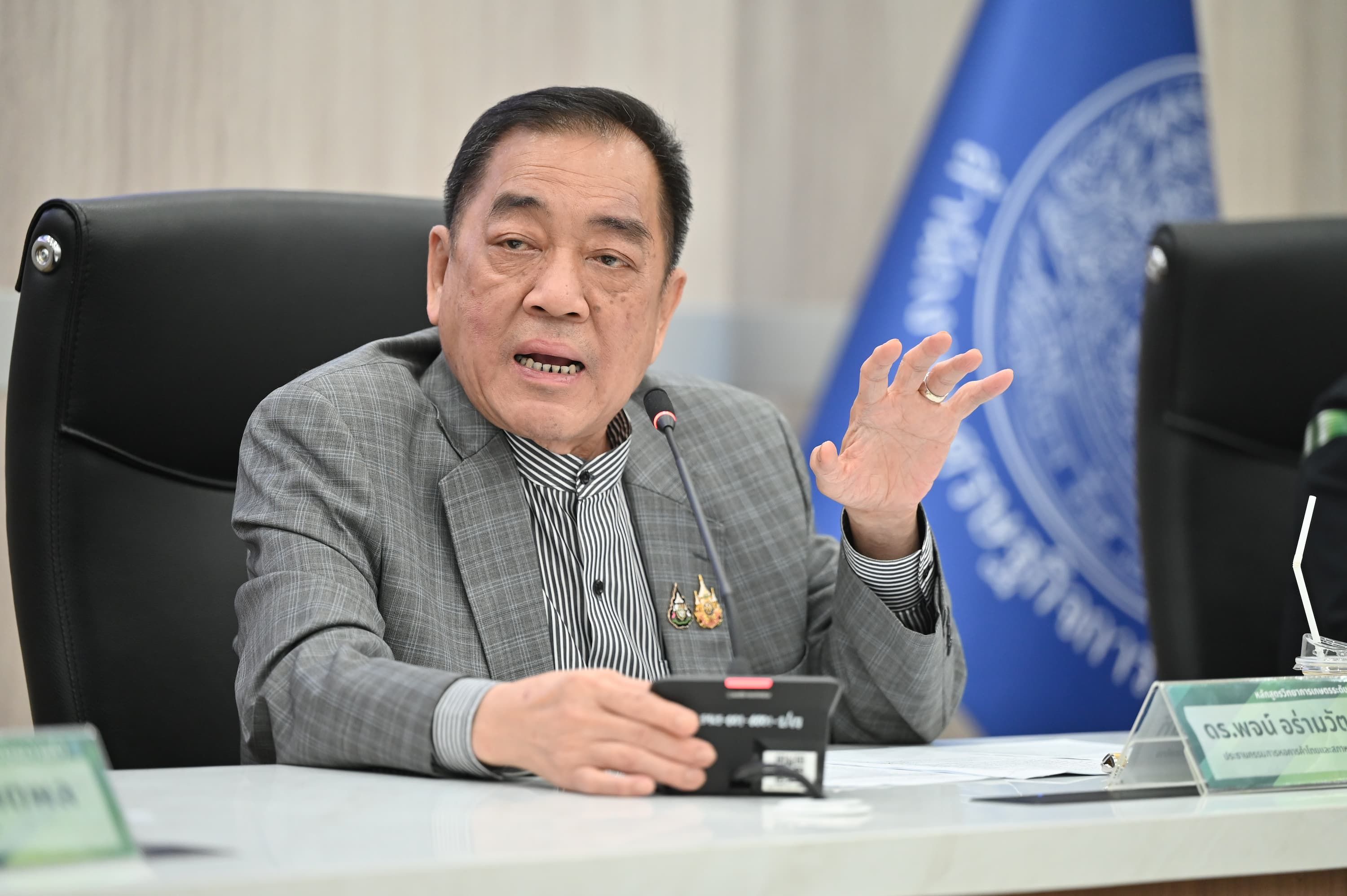 Man in gray checkered jacket gestures while speaking at a meeting table.