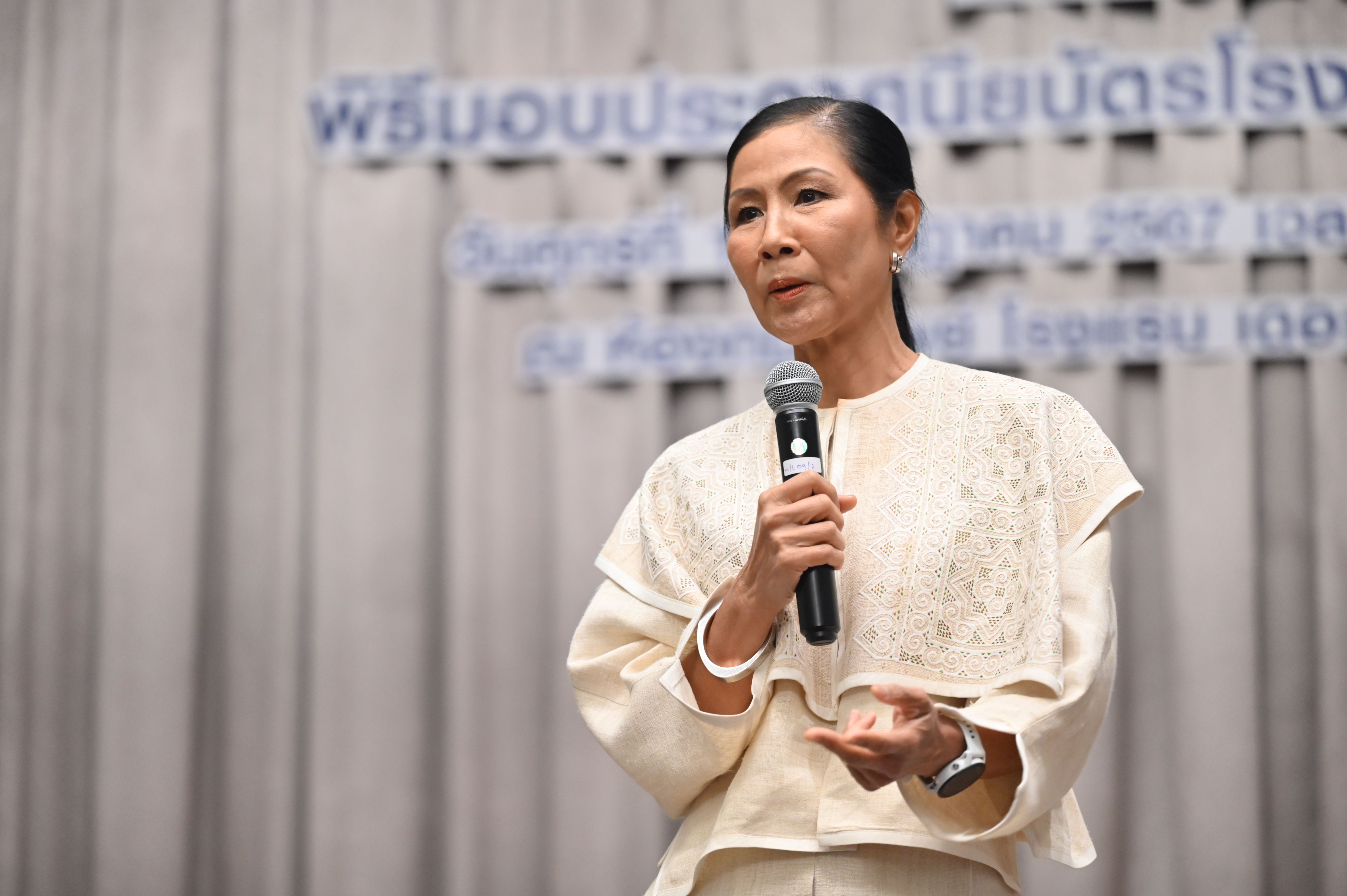 Woman in elegant light attire speaks into a microphone at a formal event.