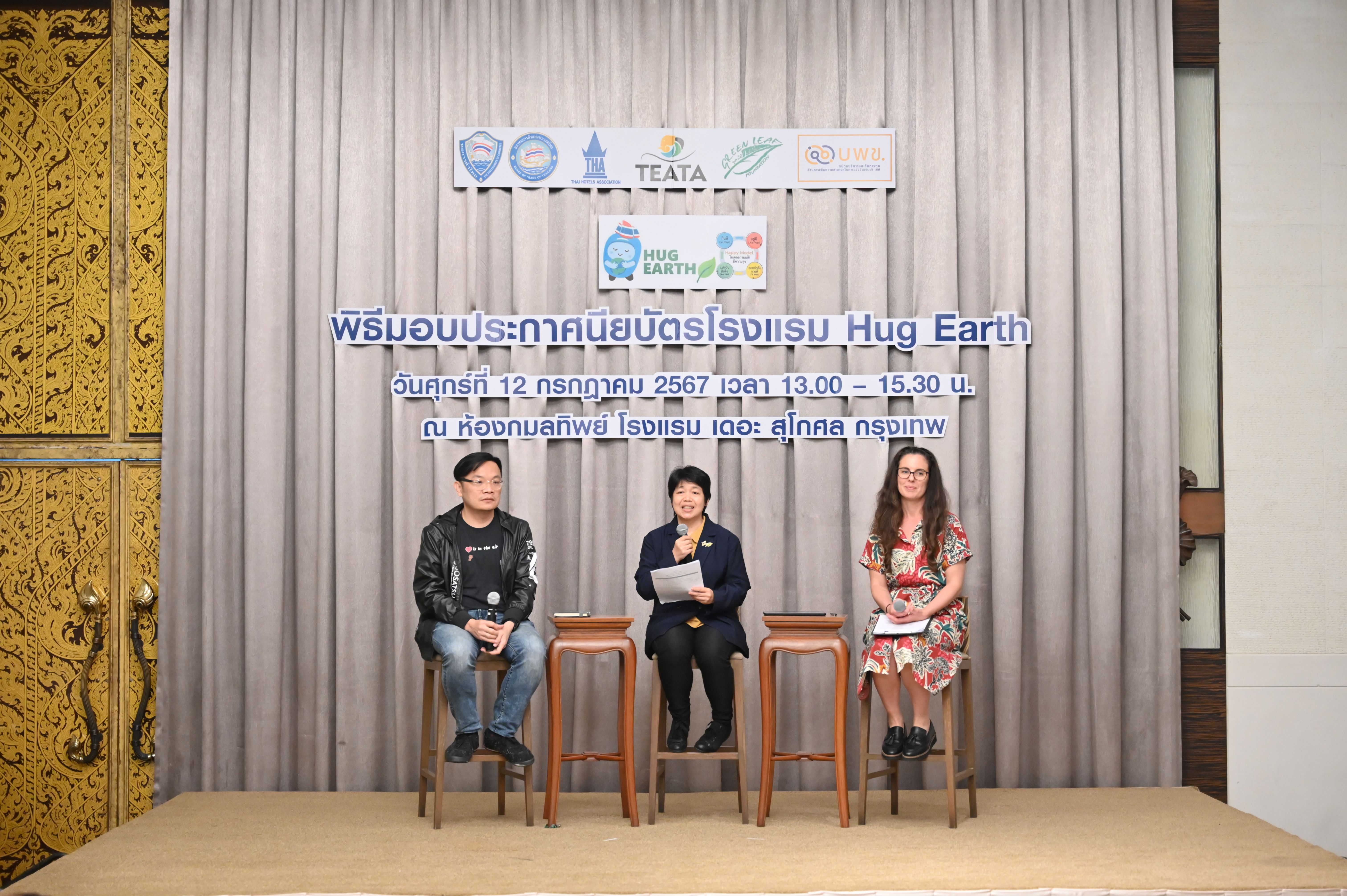 Three panelists sit on stools before a stage curtain with a "Hug Earth" banner.