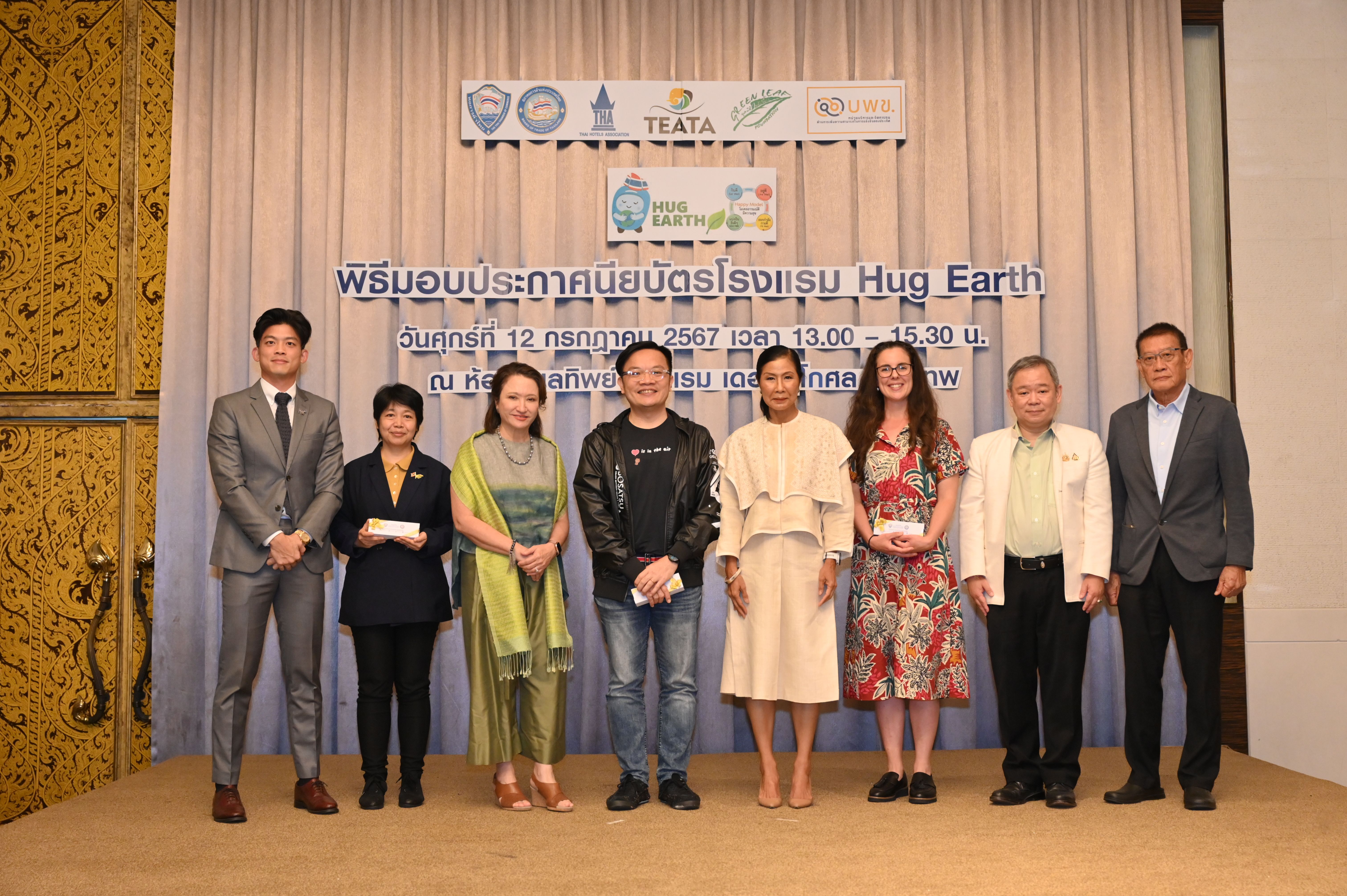 Eight people pose at a Hug Earth event with a banner in the background.