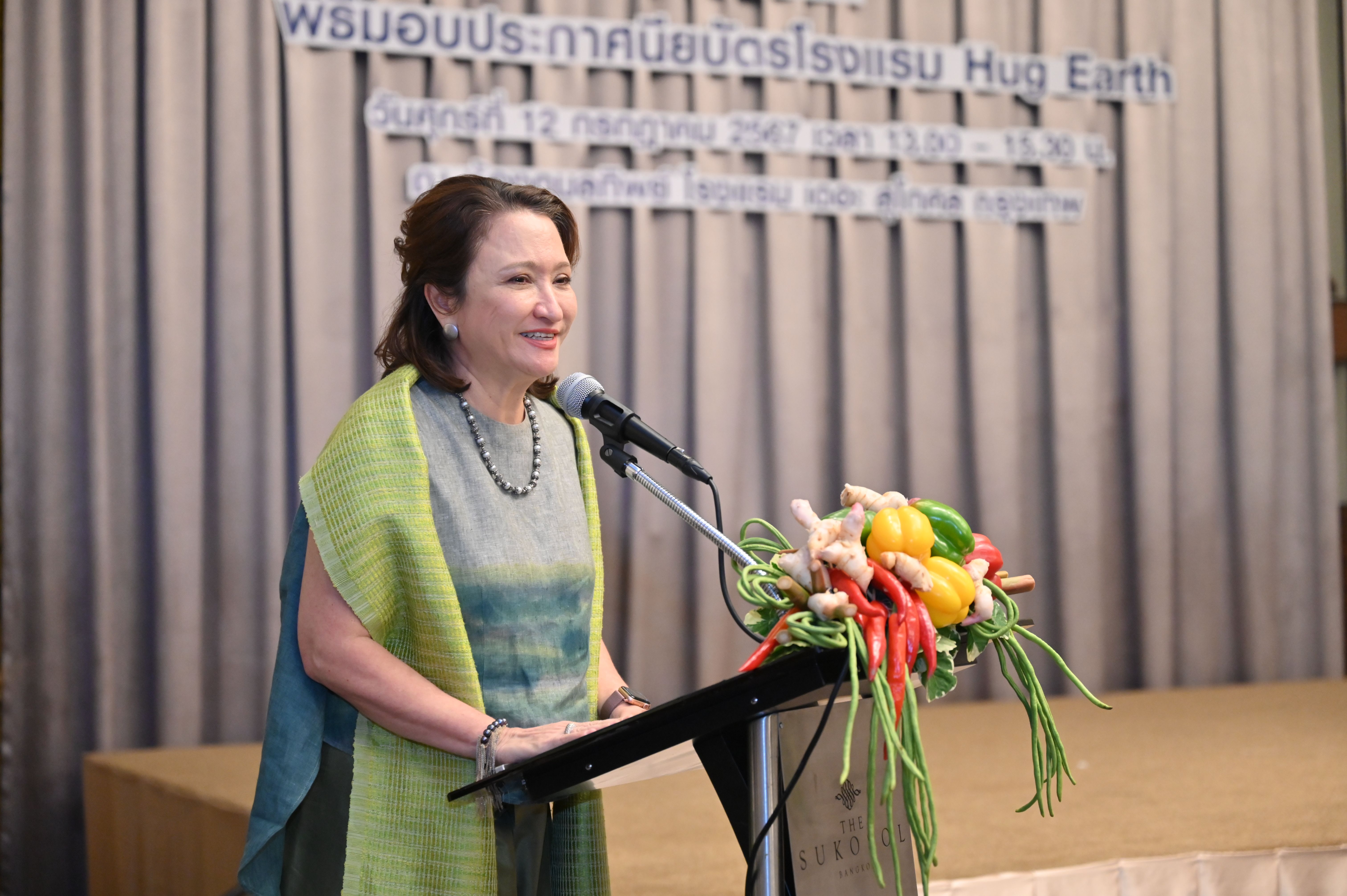 Smiling woman in traditional green attire speaks at a podium with a microphone.
