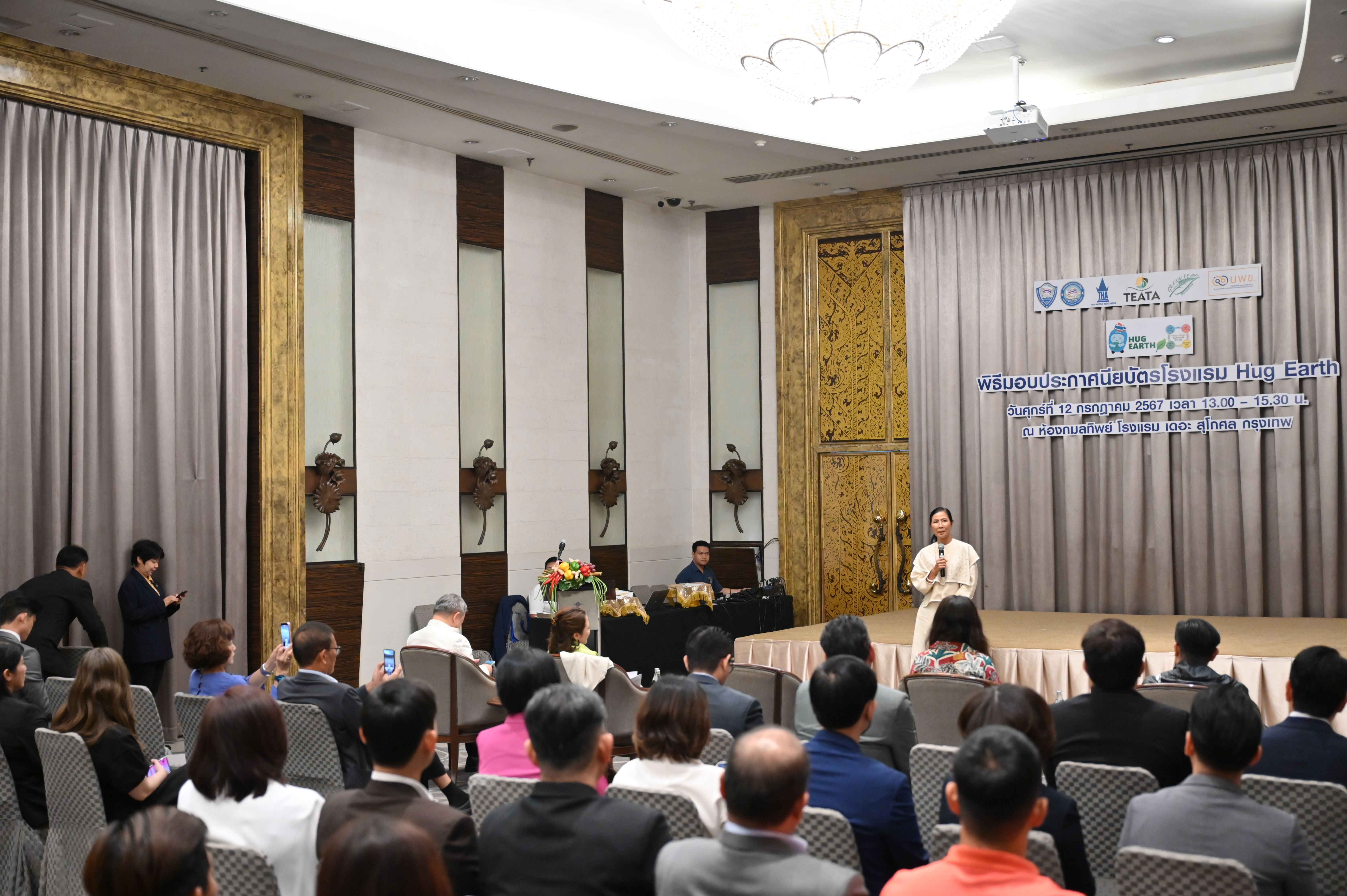A speaker addresses an audience from a stage at an indoor conference event.