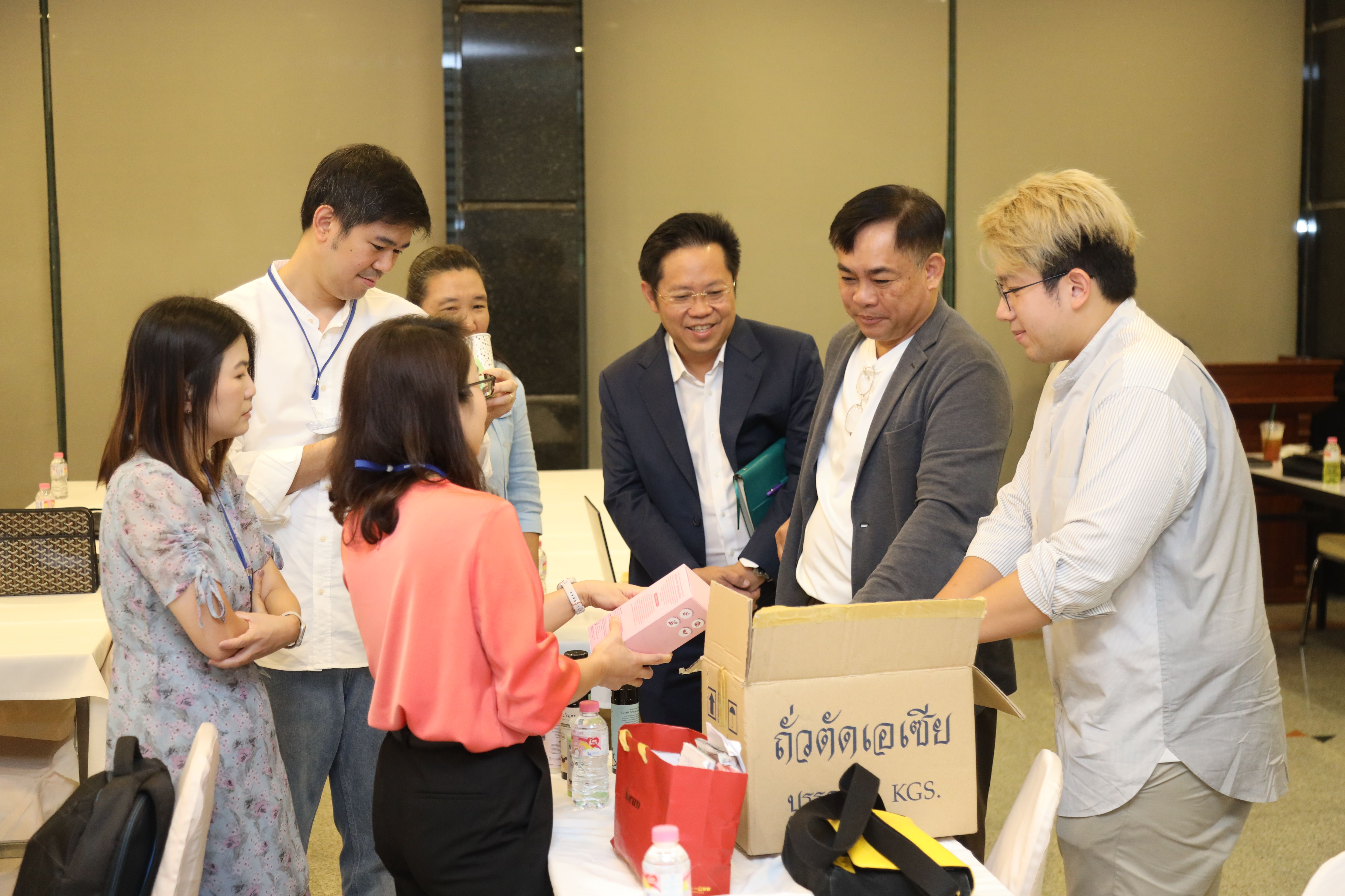 A group of people stands around a table, exchanging items from cardboard boxes indoors.