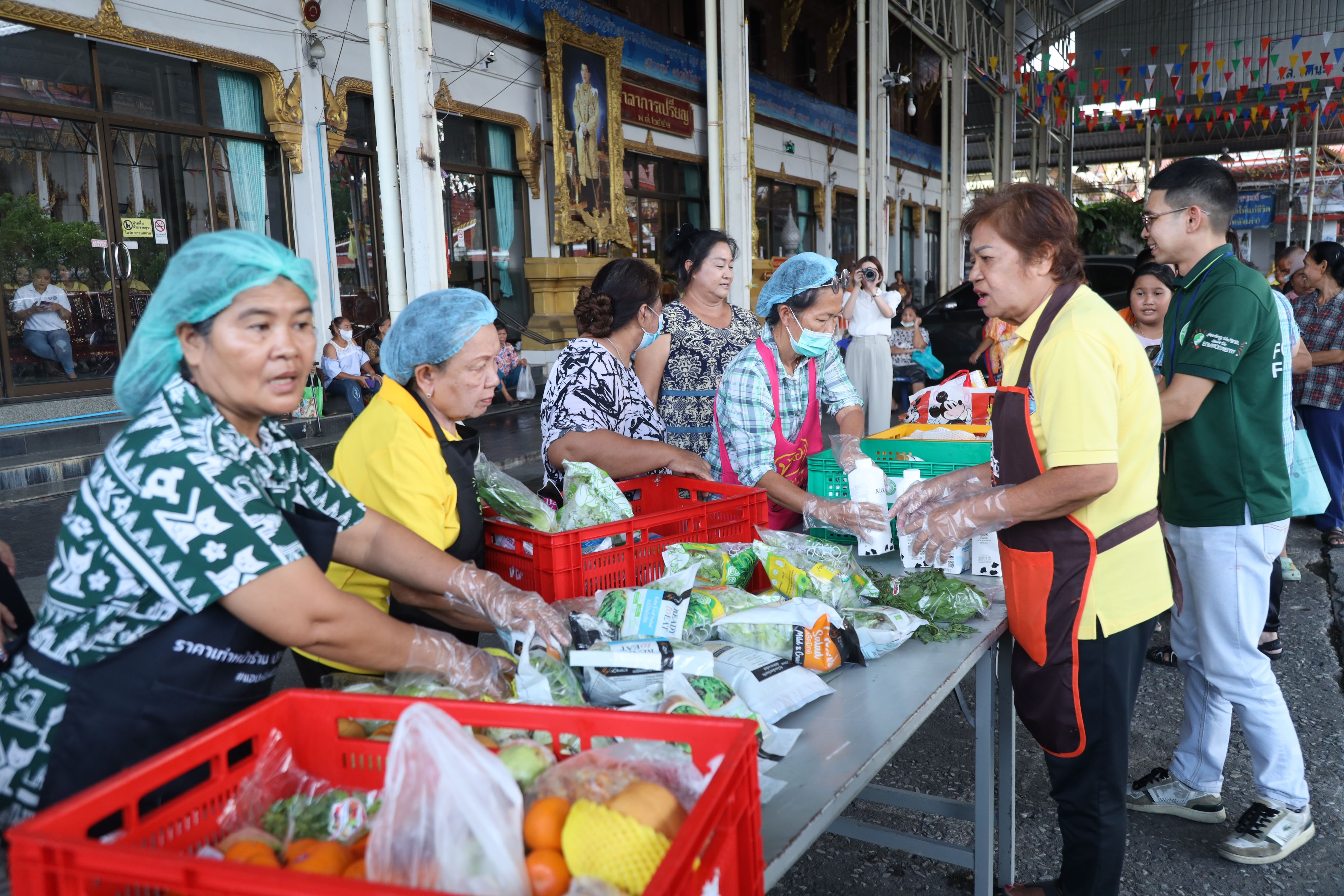Volunteers in hairnets and aprons distribute fresh produce and packaged food items at an outdoor event.