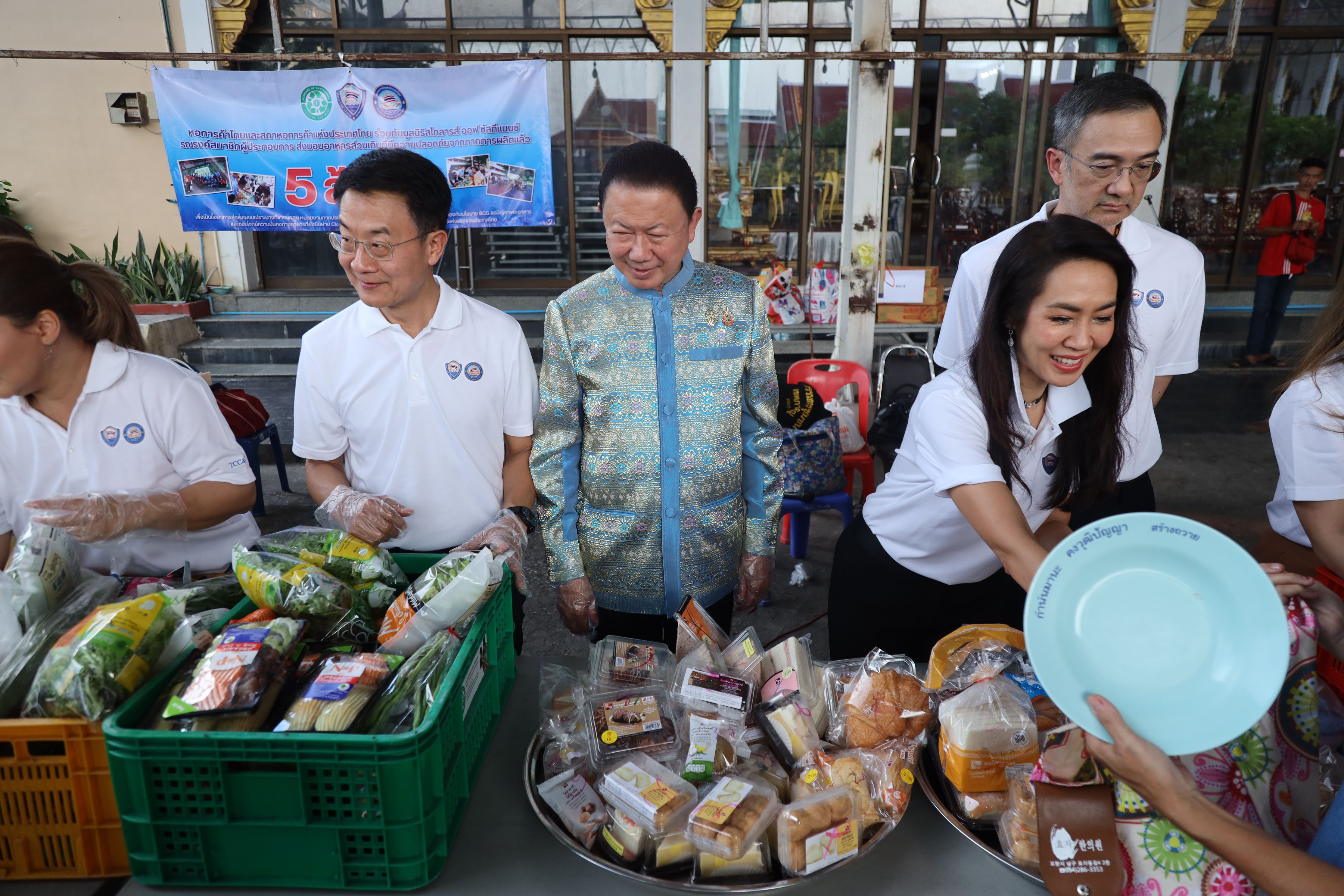 People distribute food and packaged items from tables at a community event.