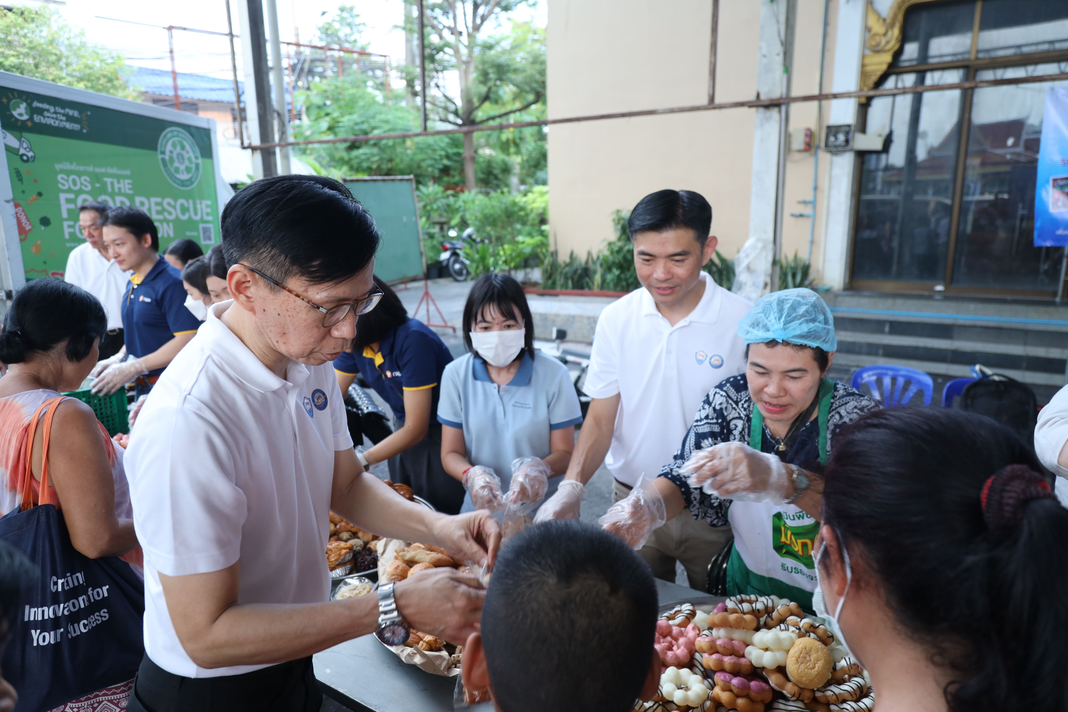 Volunteers distribute various pastries and donuts to people at an outdoor community event.