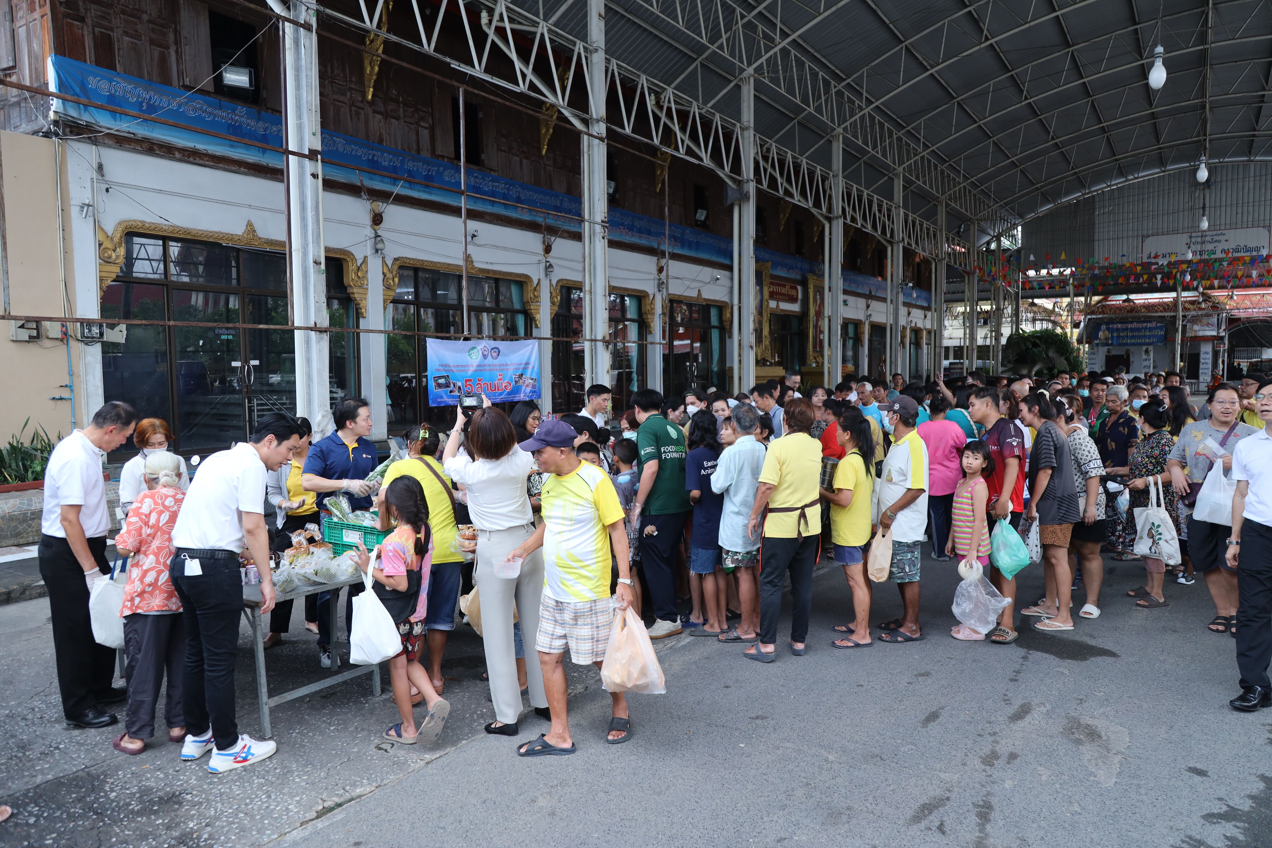 A long line of people receive supplies from volunteers under a large covered area.