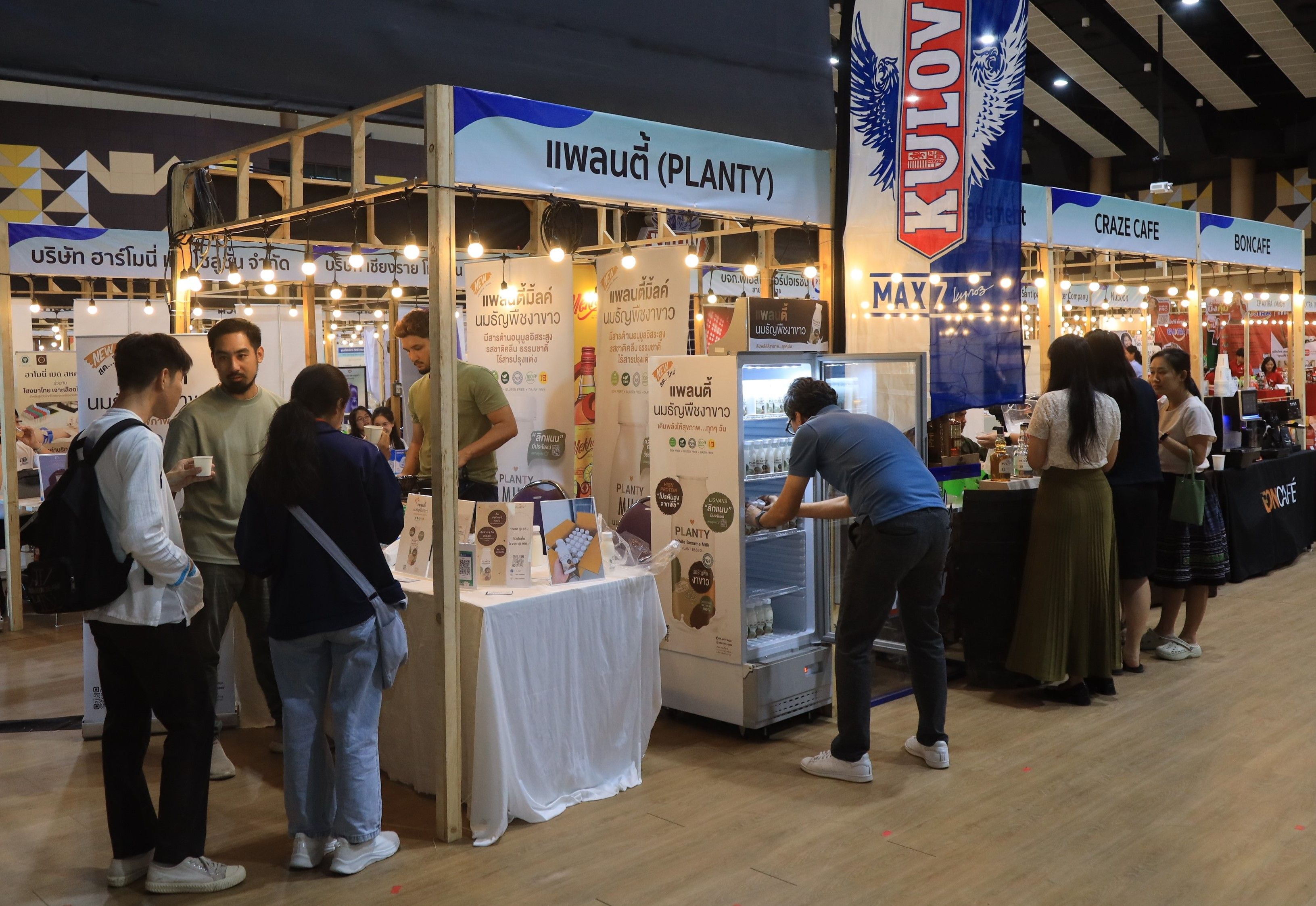 People browsing various product stalls at a bustling indoor exhibition, featuring food and beverage vendors.
