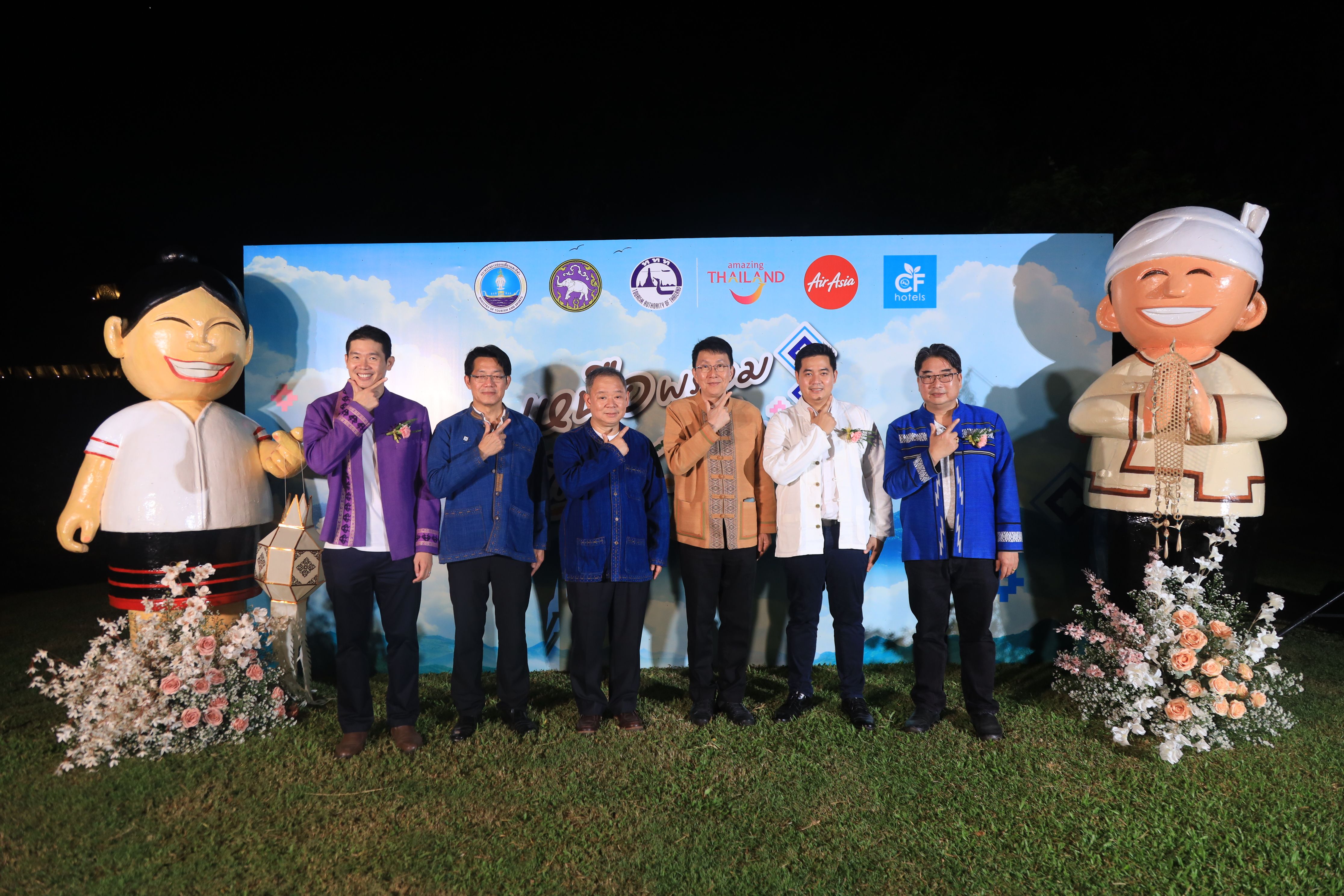 Six men pose with two large cartoon figures in front of a blue banner at an outdoor event.