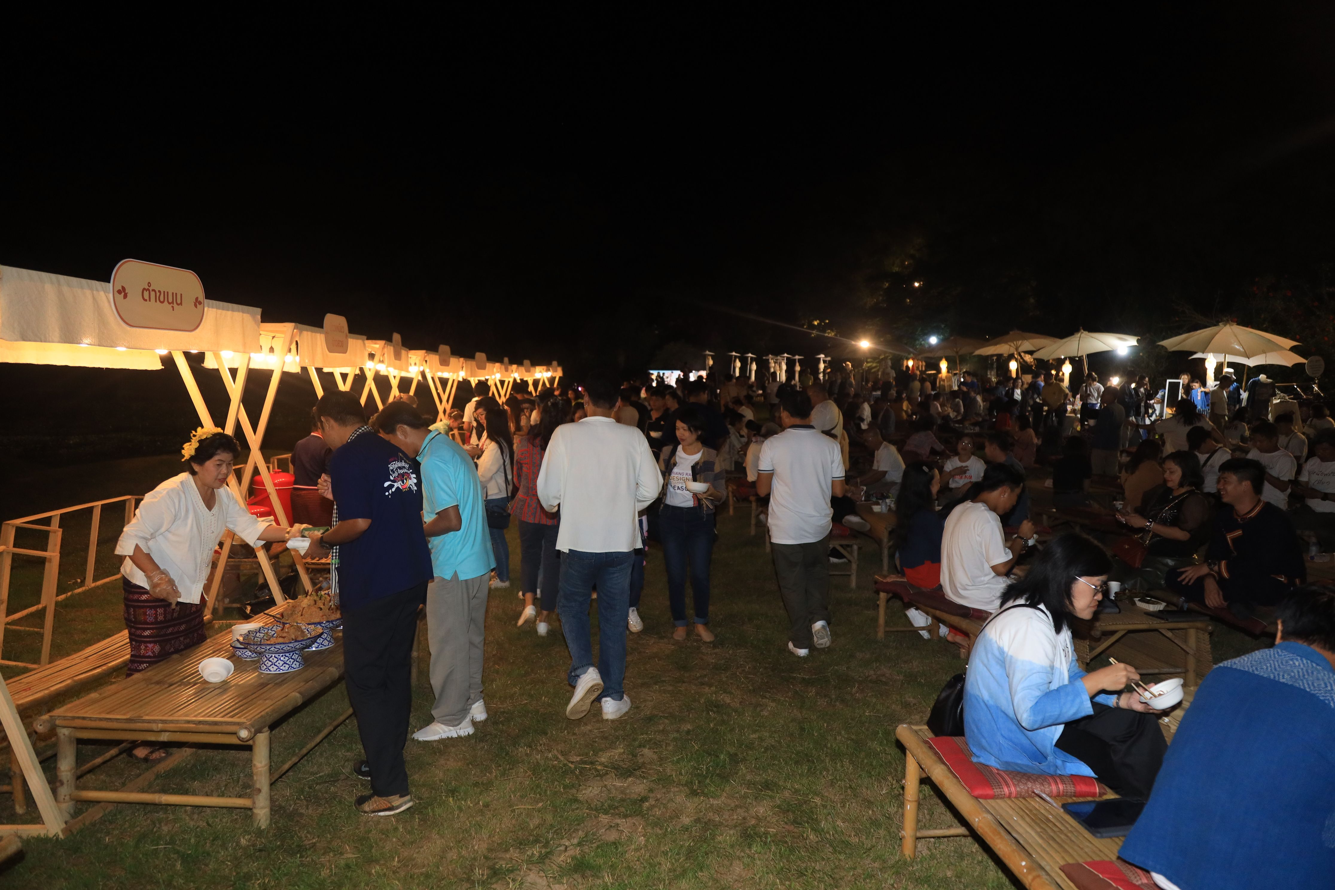 Many people gather at a lively outdoor night event with illuminated food stalls.