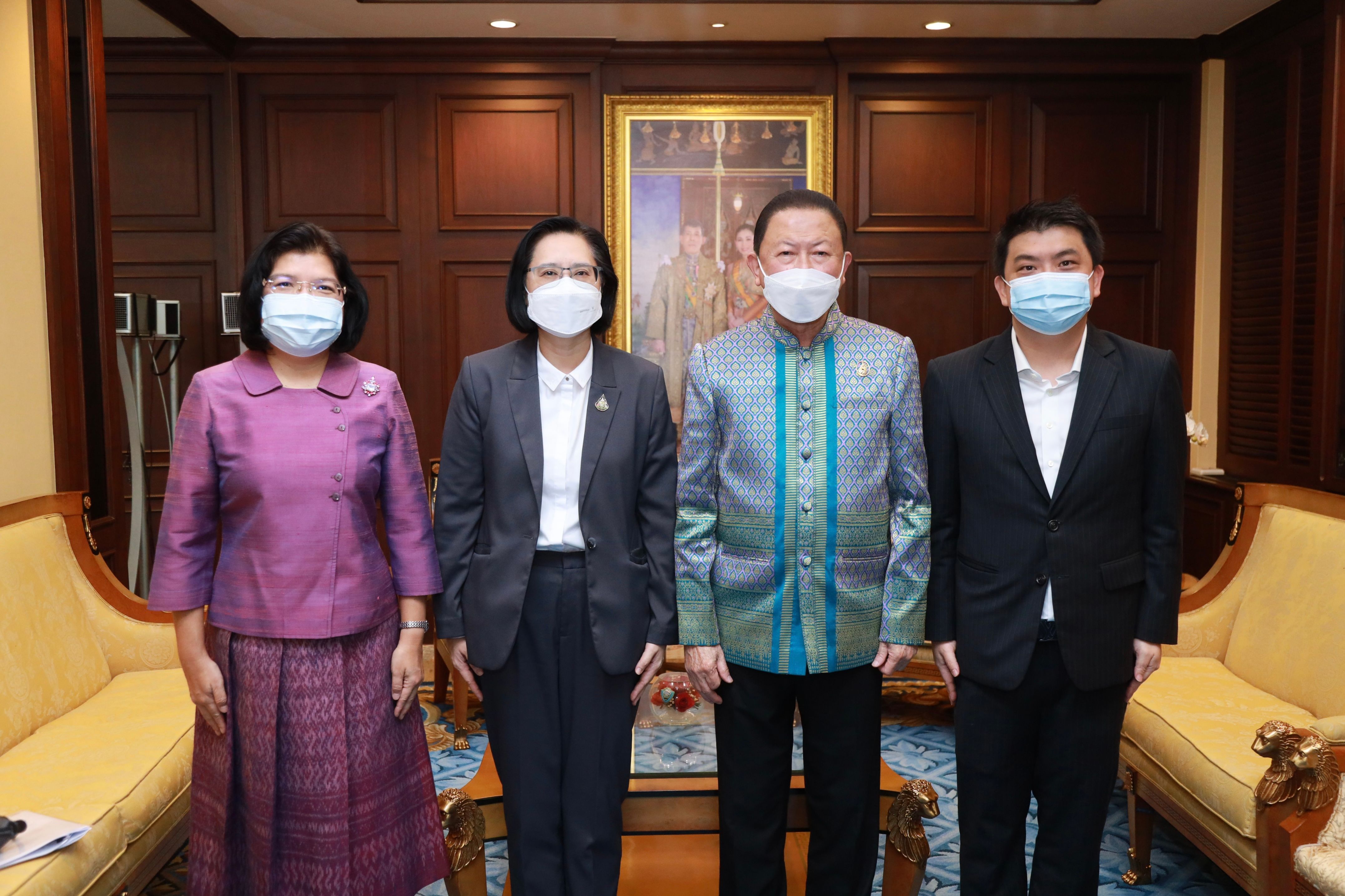 Four people in masks, two men and two women, stand together in a formal room.