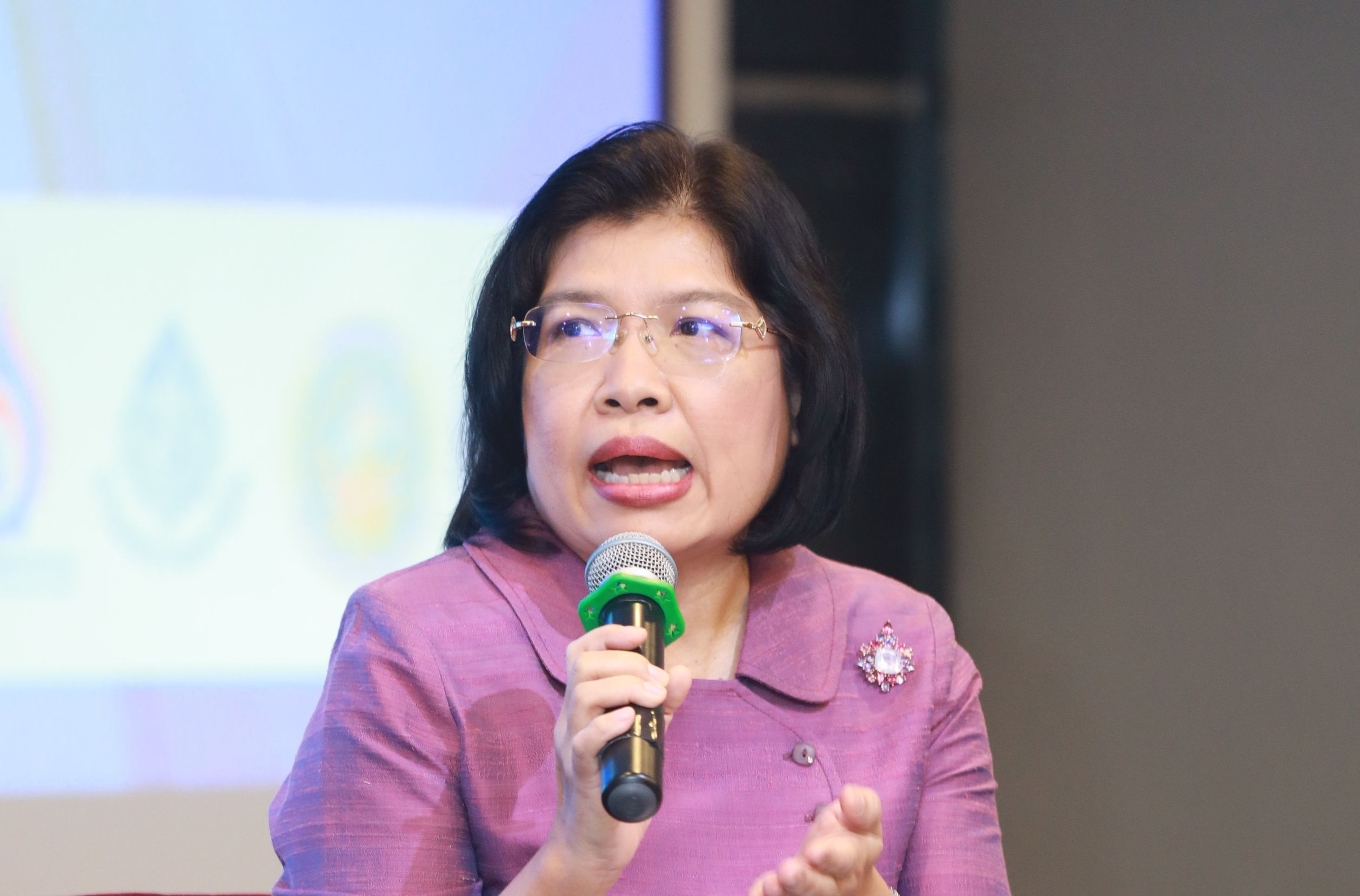 Woman with glasses speaks into a microphone during a presentation.