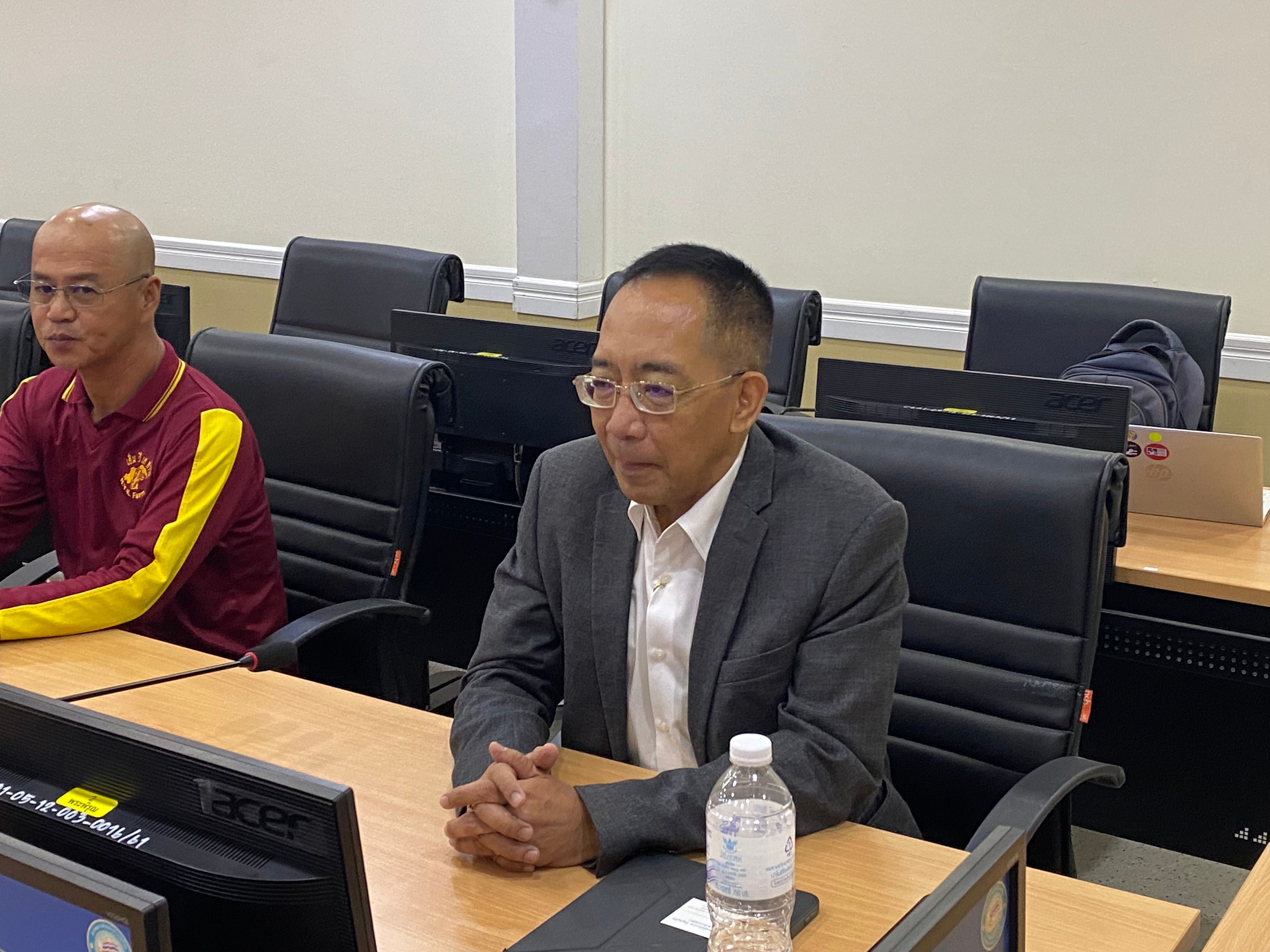 A man in a suit and glasses sits at a conference table, attending a meeting.