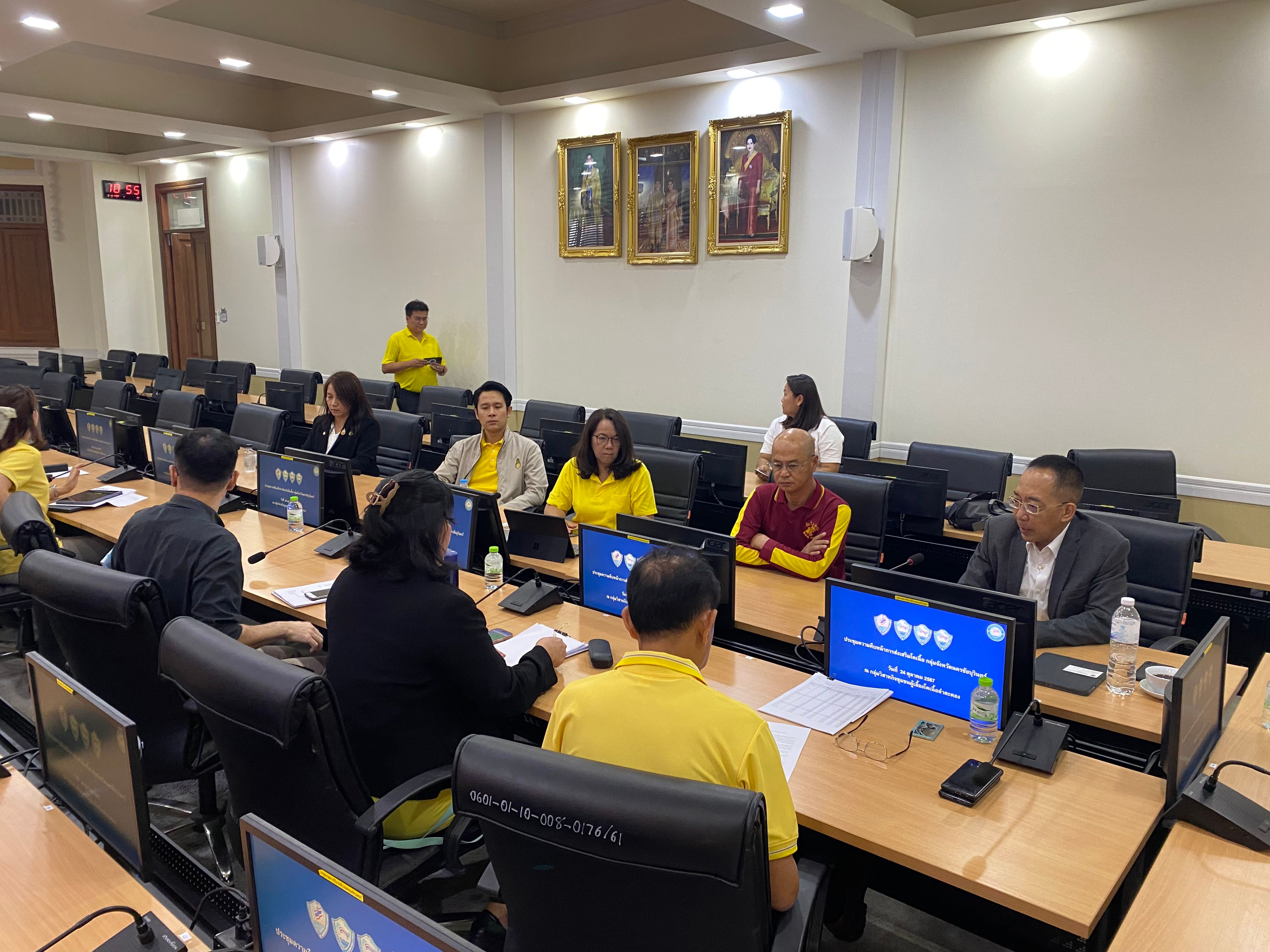 Group of people attend a professional meeting around a conference table with computer screens.