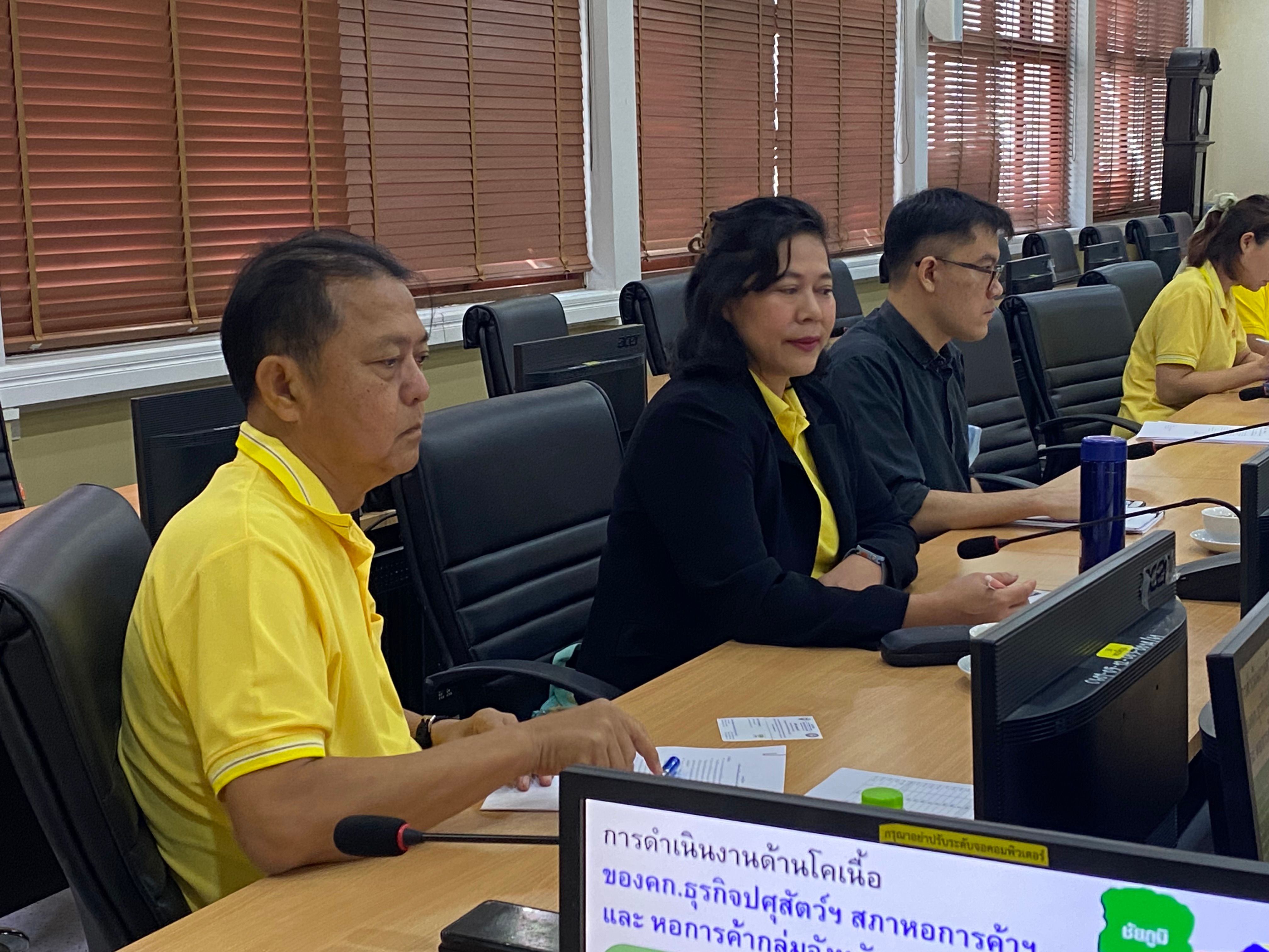 Attendees in yellow shirts and dark attire sit around a long conference table.