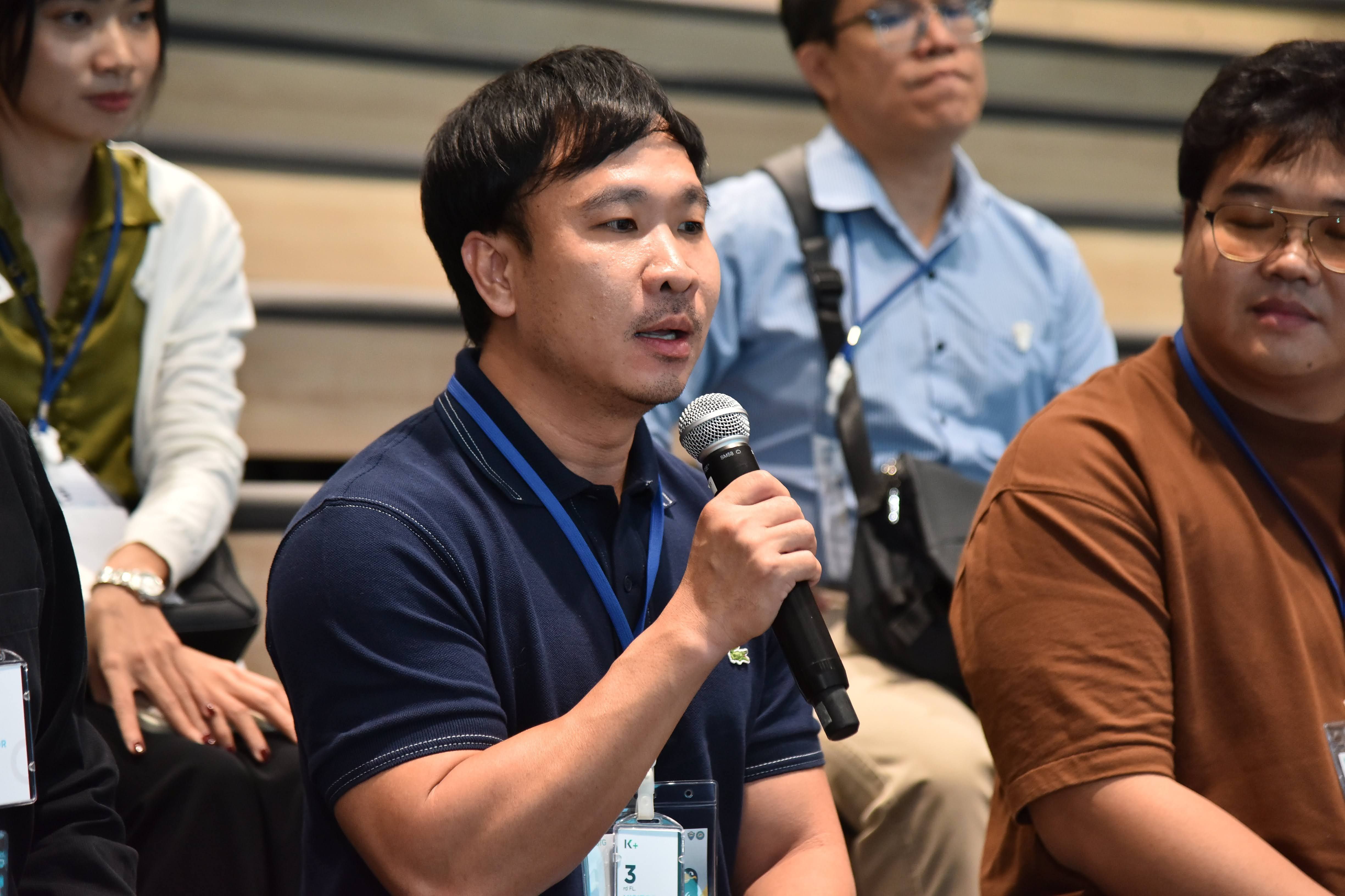 Man in blue polo shirt speaks into a microphone at an event.