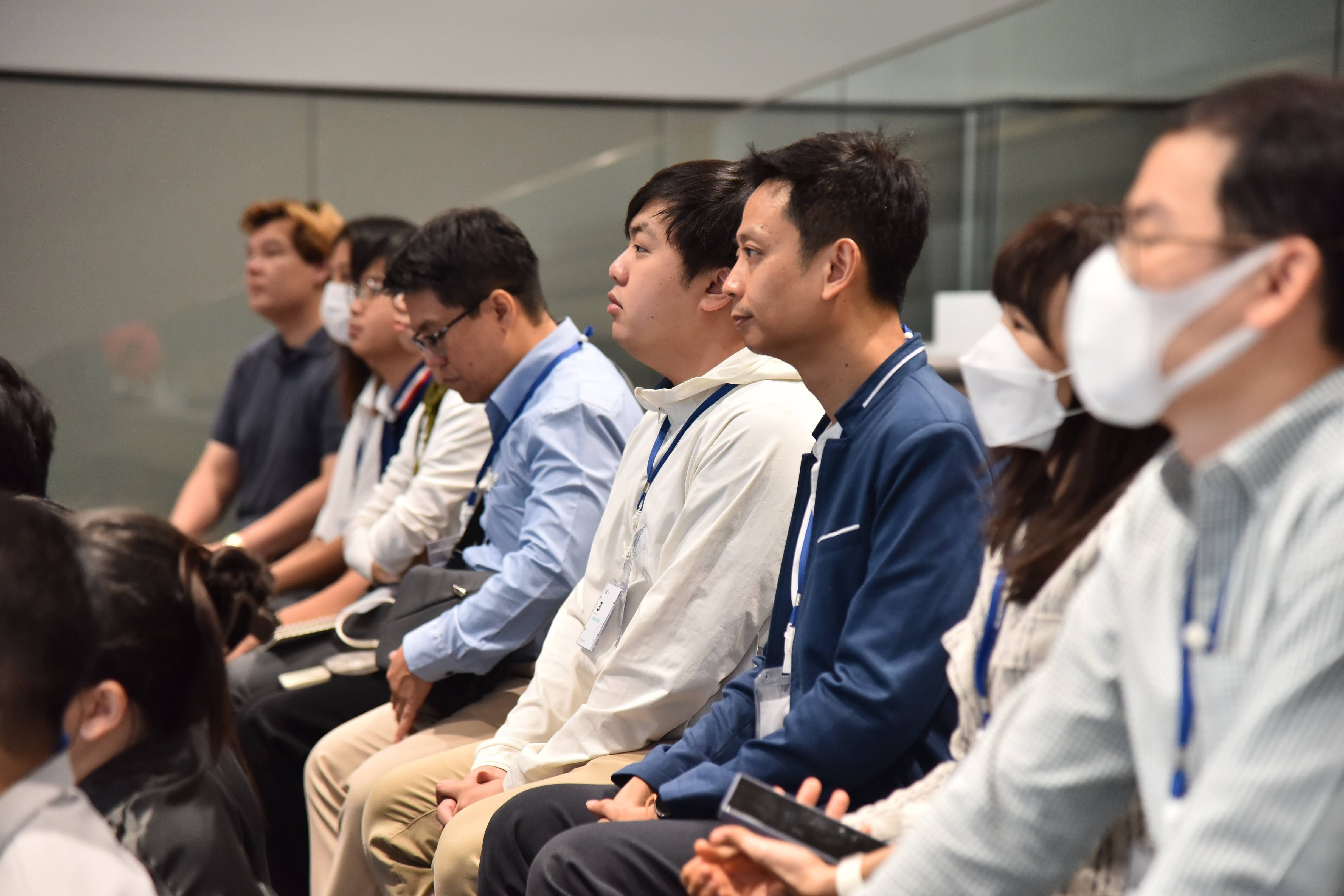 A diverse group of East Asian people attentively sit in an audience at an indoor event.