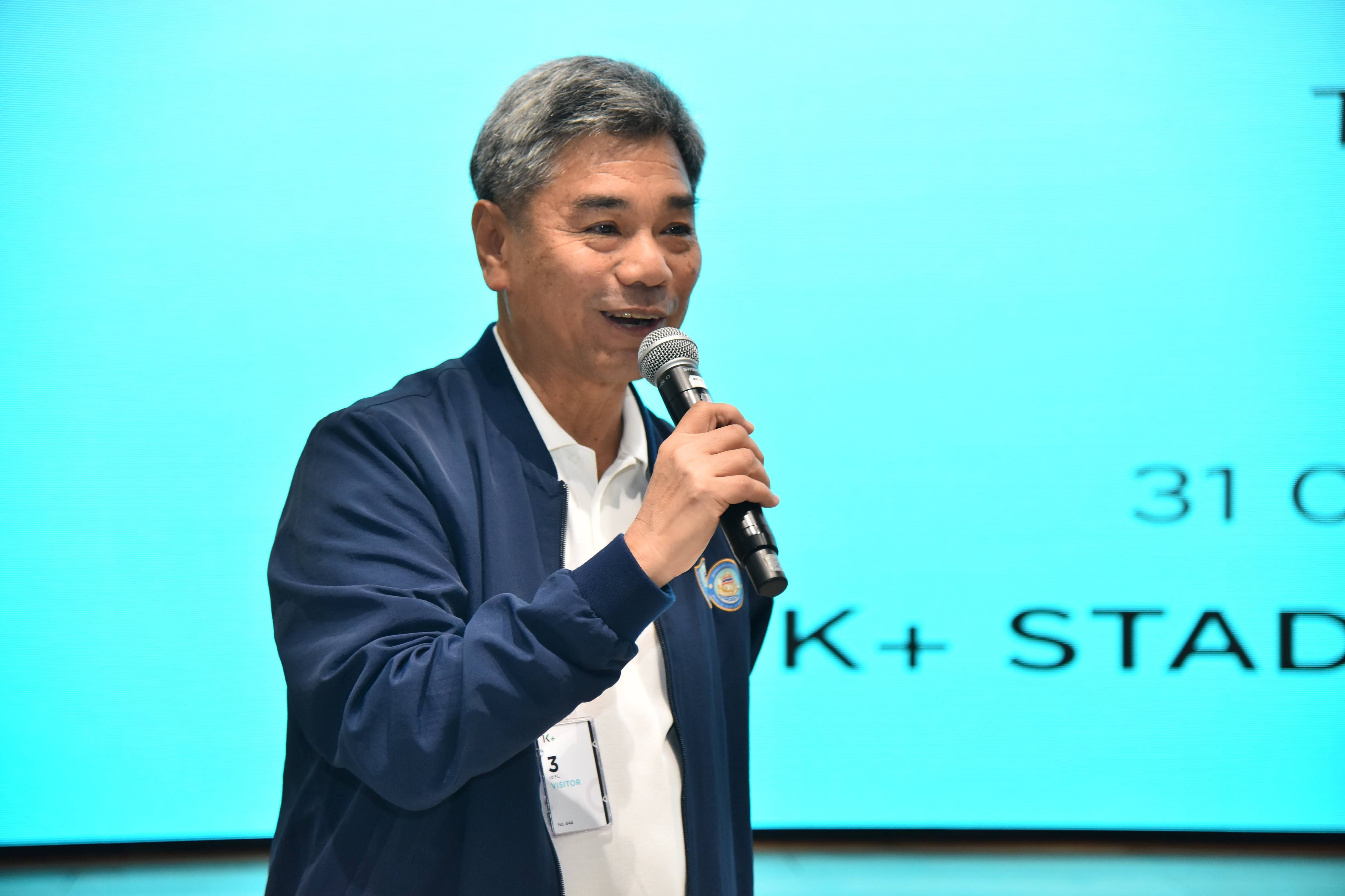 Middle-aged Asian man with grey hair speaking into a microphone at an event.