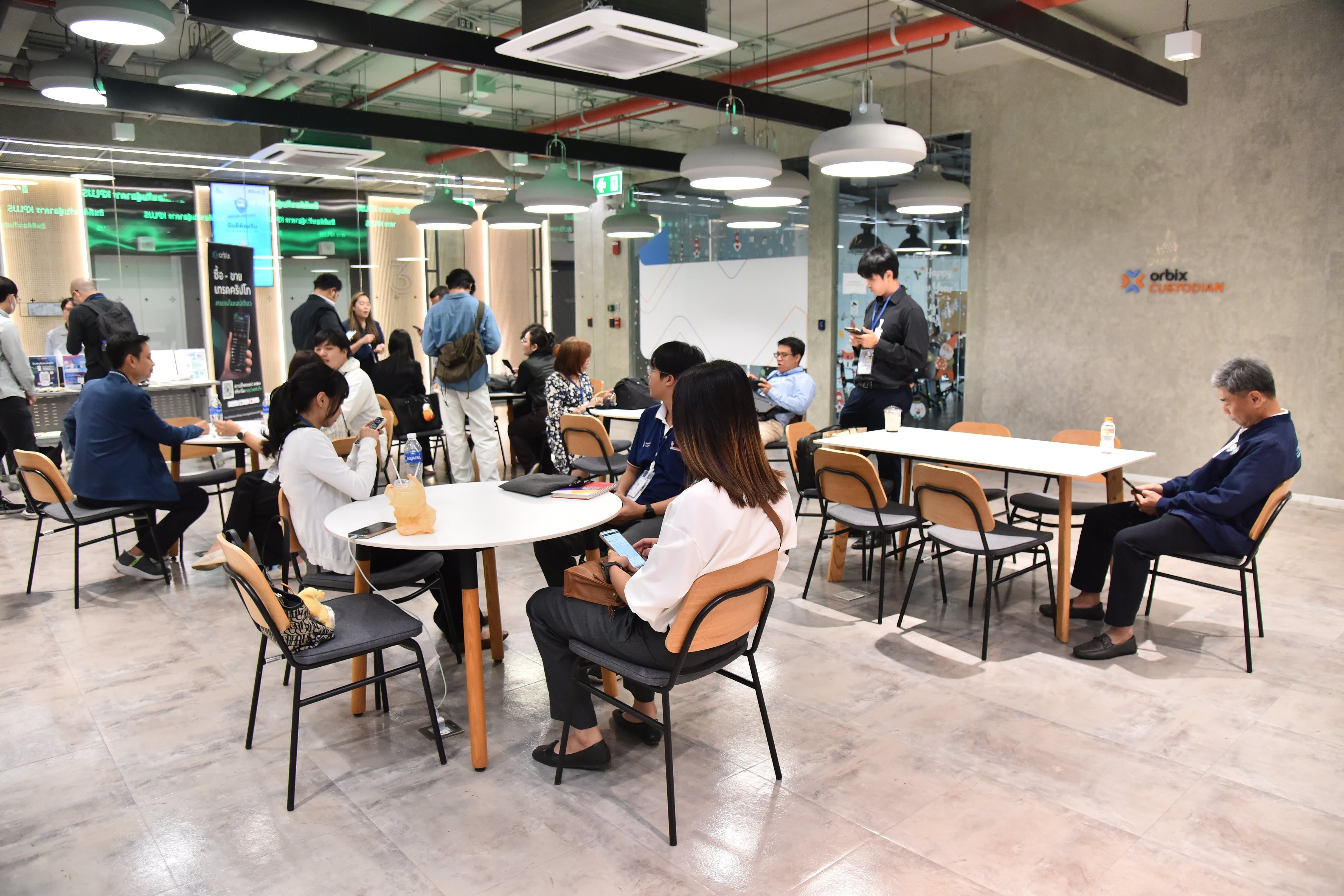 People gathered in a bright, modern office common area with tables and chairs.
