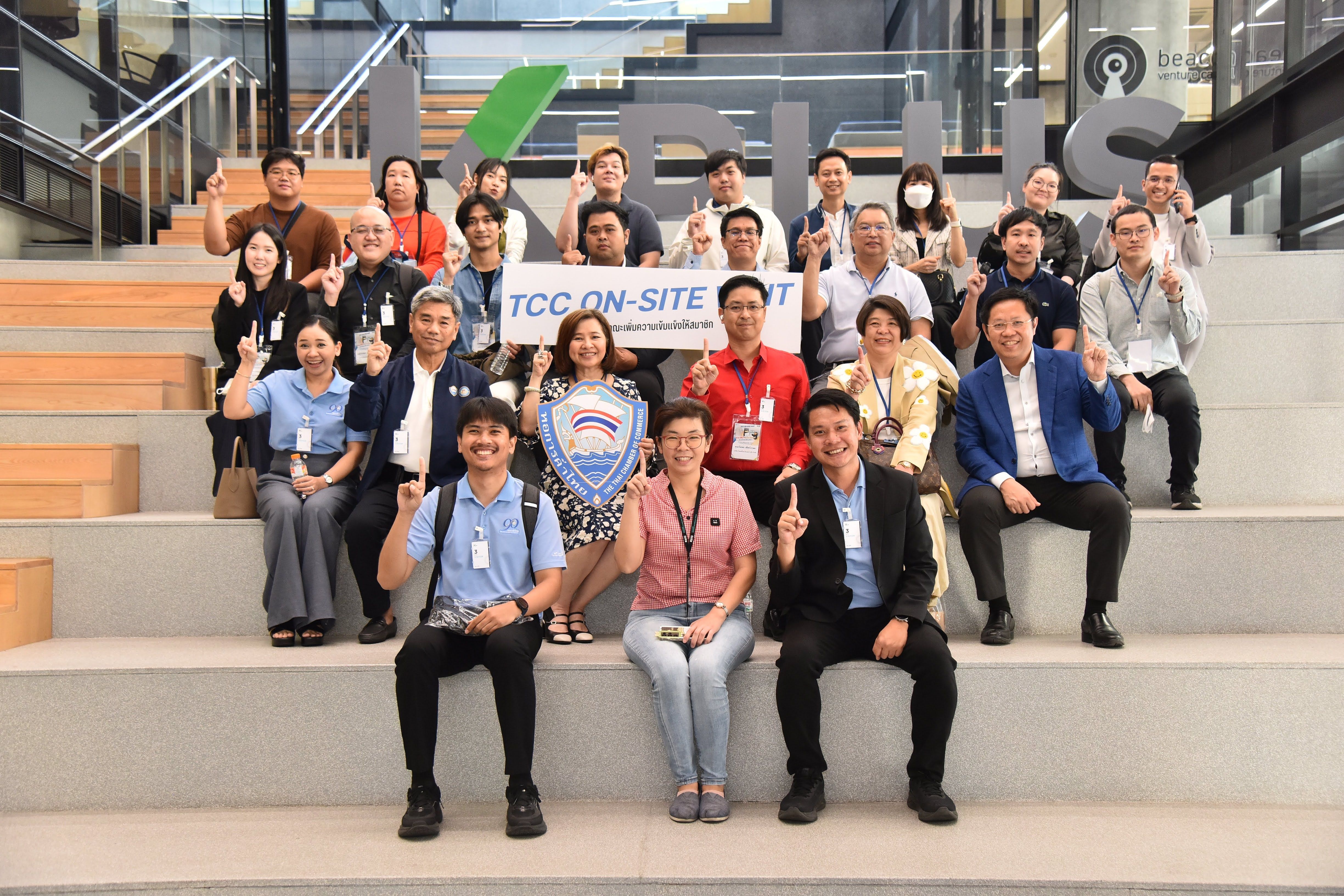 Diverse group of people smiling, holding an 'FCC ON-SITE' banner on modern steps.