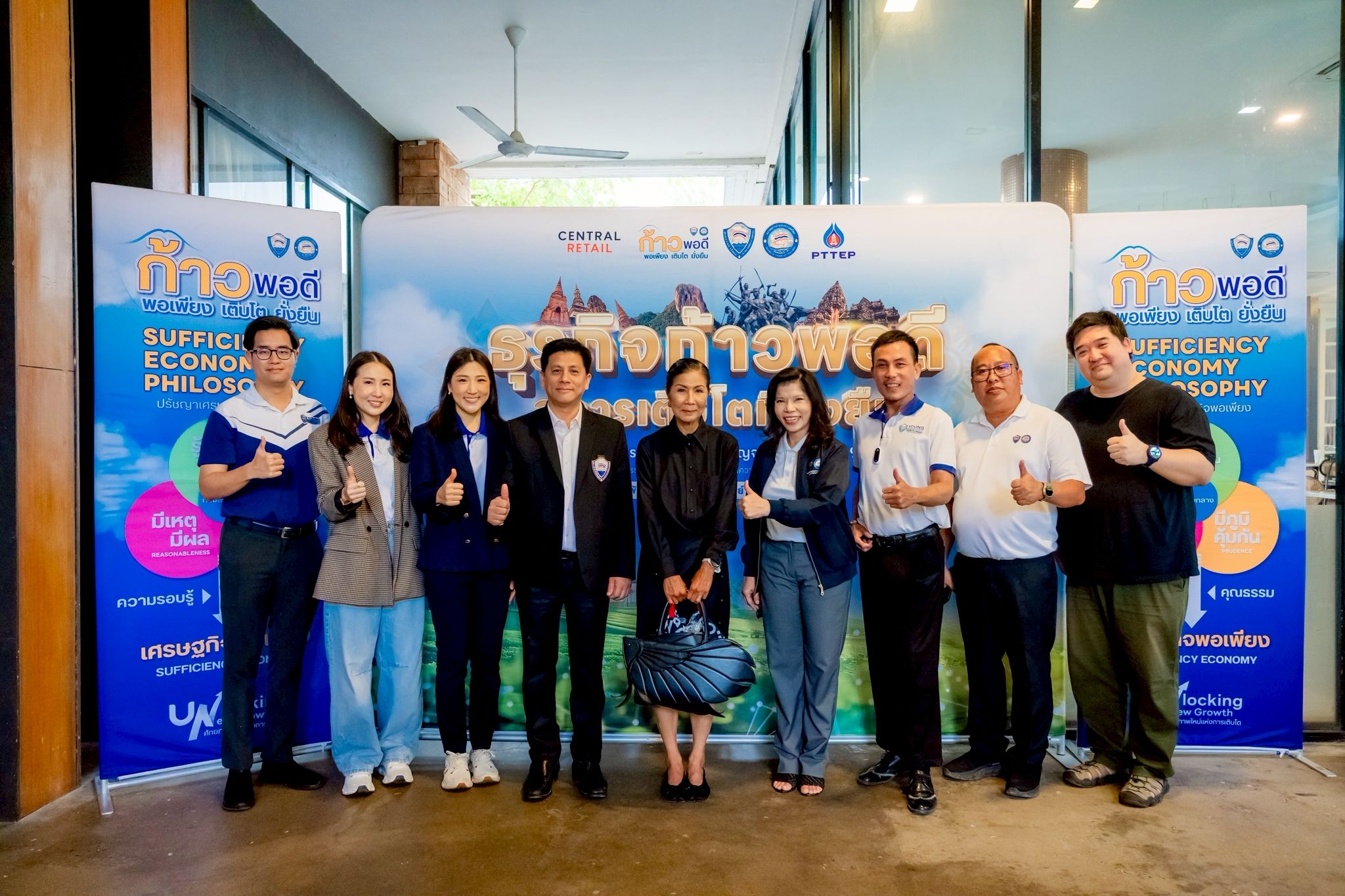 Group of ten smiling individuals giving thumbs up in front of an event banner.