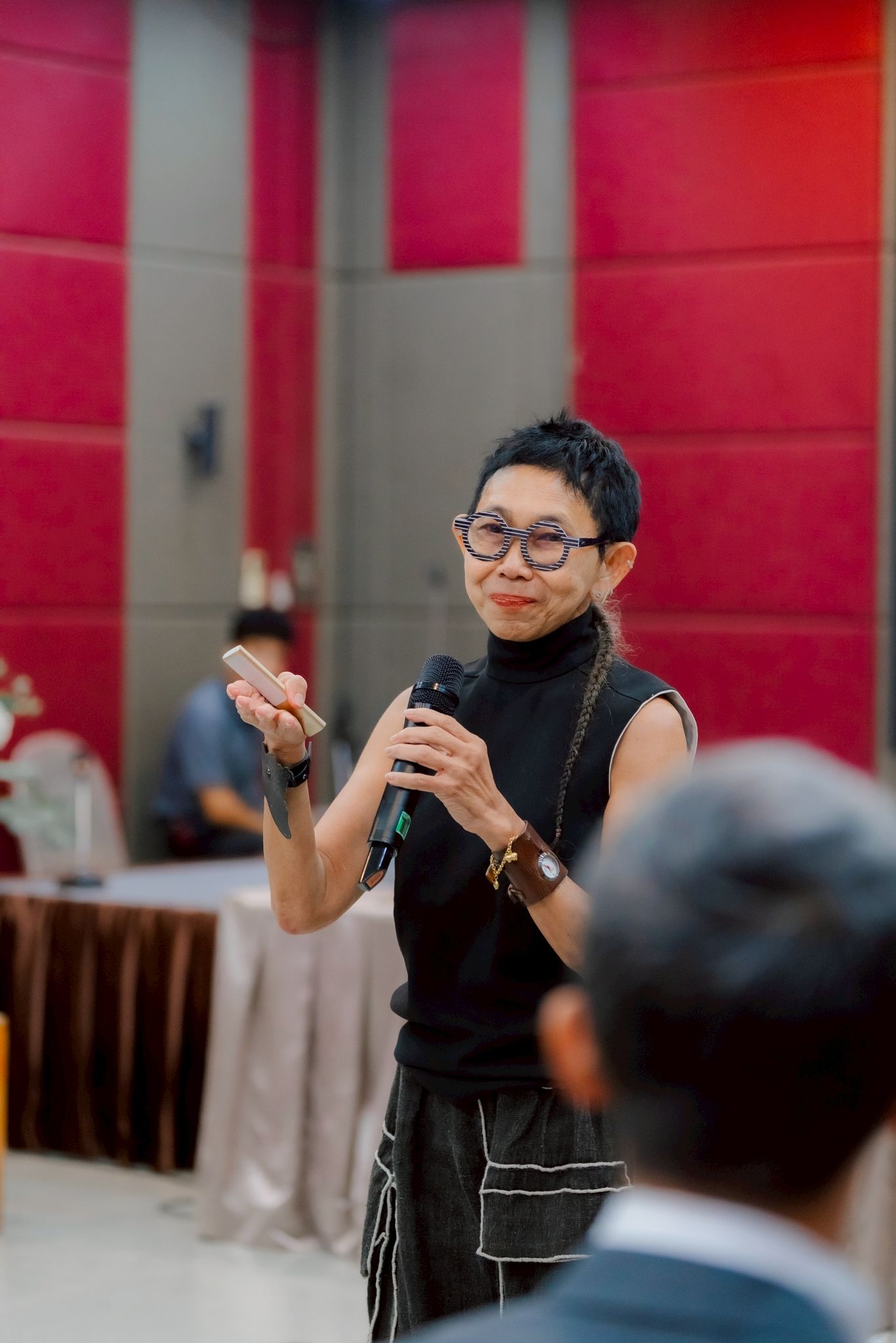 Woman with short hair and glasses presenting at a conference, gesturing with hands.