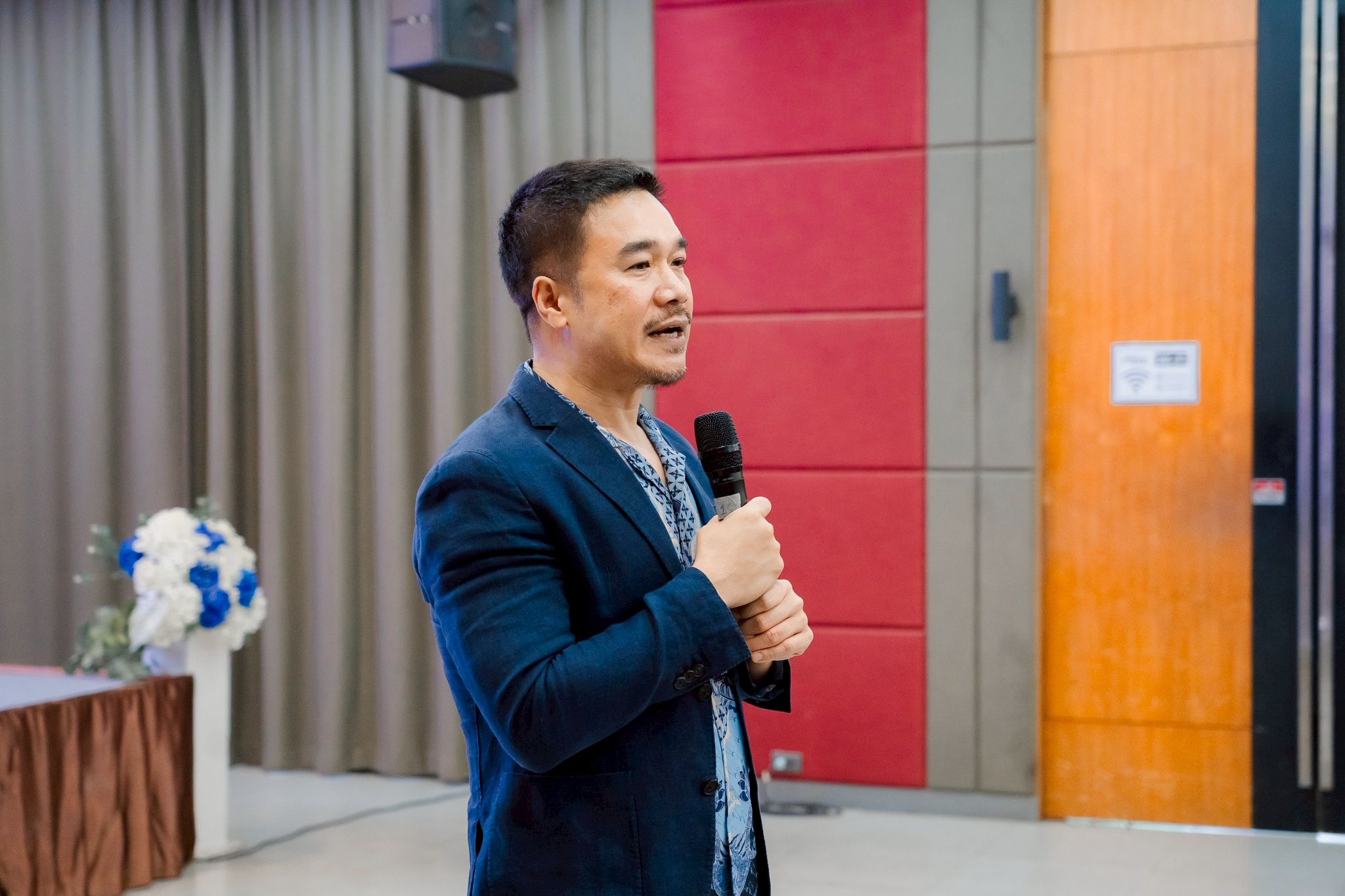 A man in a blue jacket speaks into a microphone at a formal event.