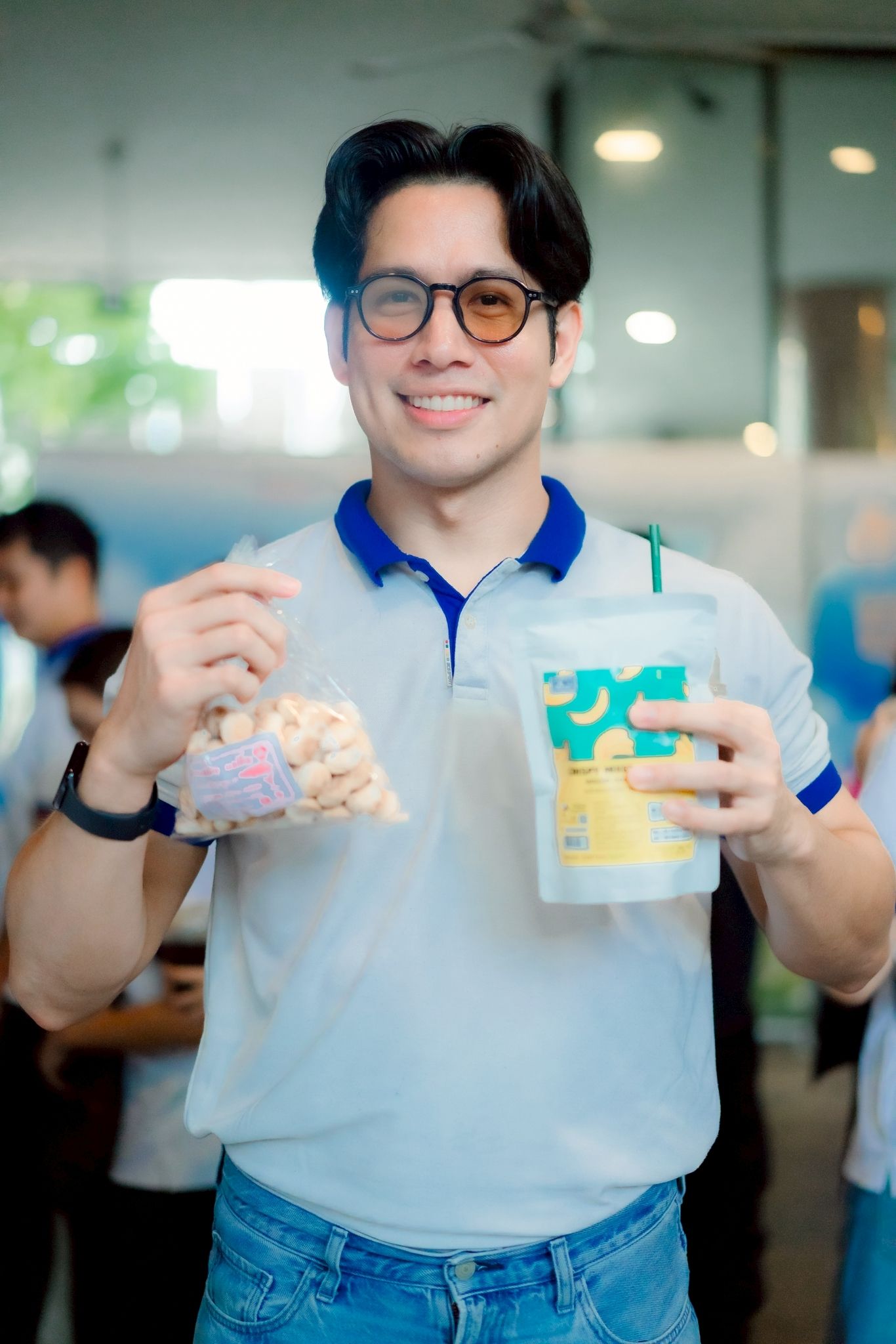 Smiling man in glasses holding a bag of popcorn and a large drink cup.