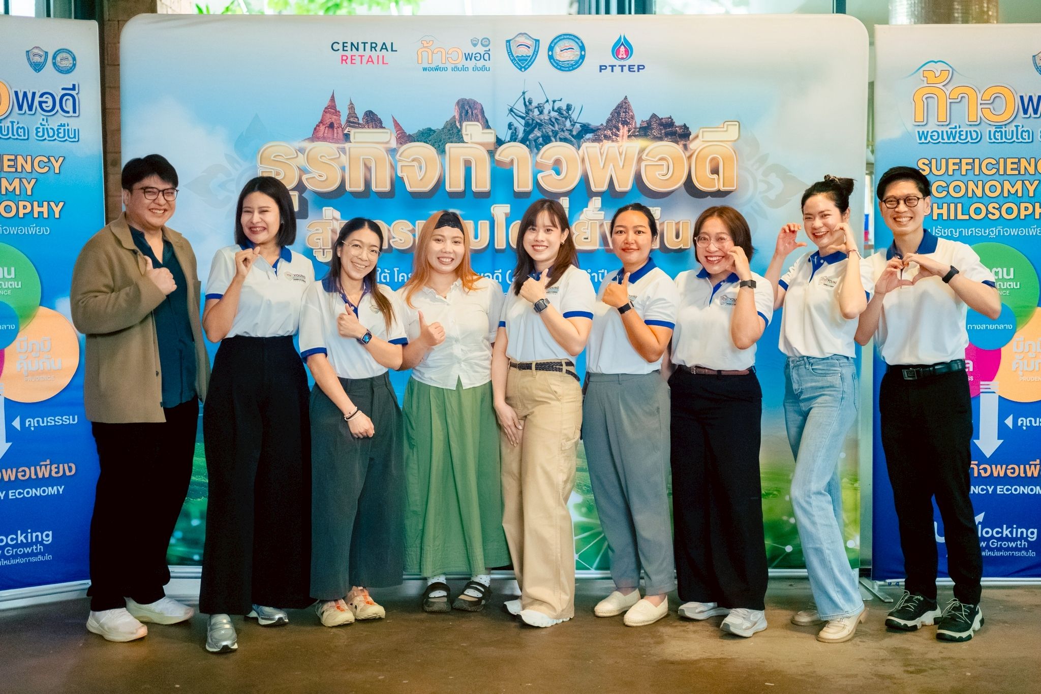 Eight young people pose cheerfully in front of a banner about sufficiency economy.