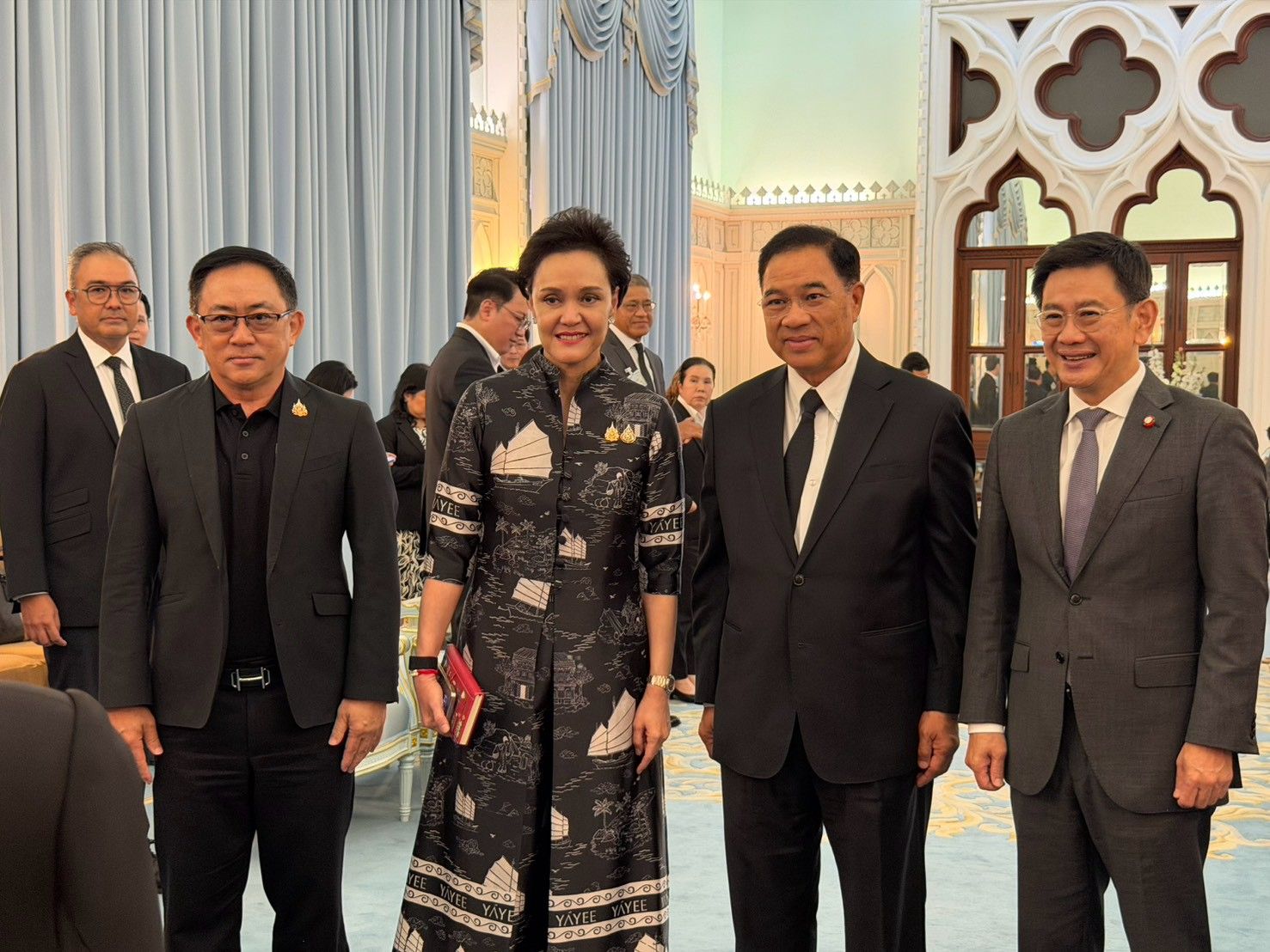 Three men and one woman in formal attire pose together at an indoor event.