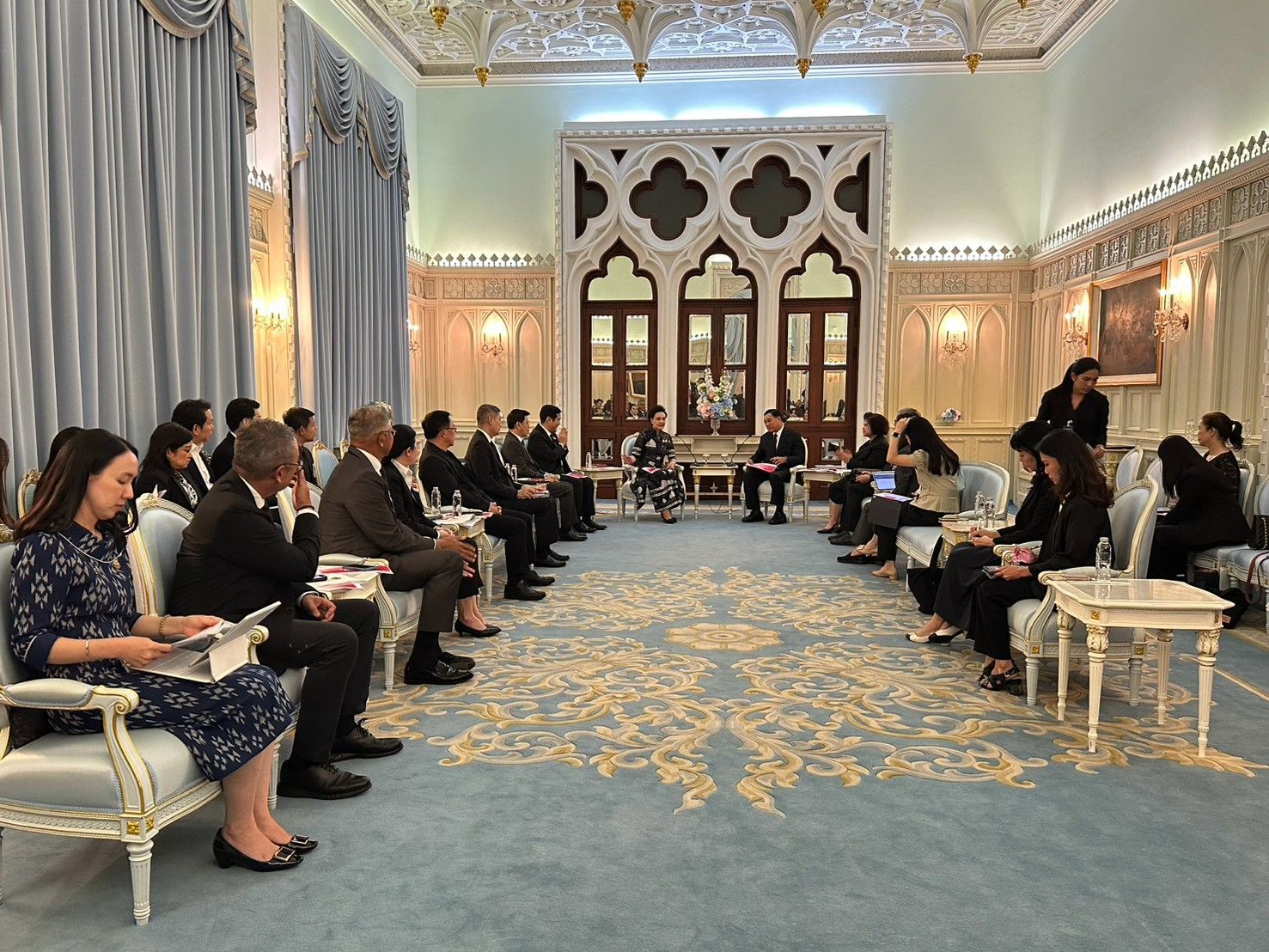 Delegates sit in an ornate room, engaged in a formal meeting and discussion.