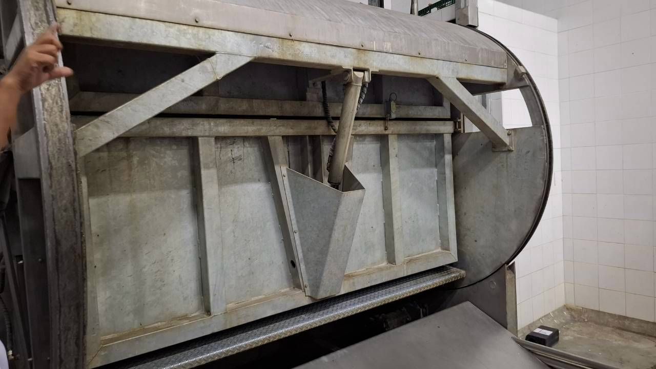 Industrial metal machine with an open lid revealing internal compartments, hand on left.