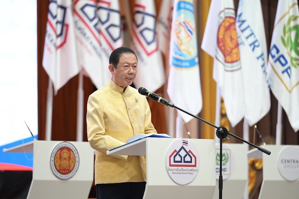 Man in yellow traditional attire speaks at a podium before a display of organizational flags.