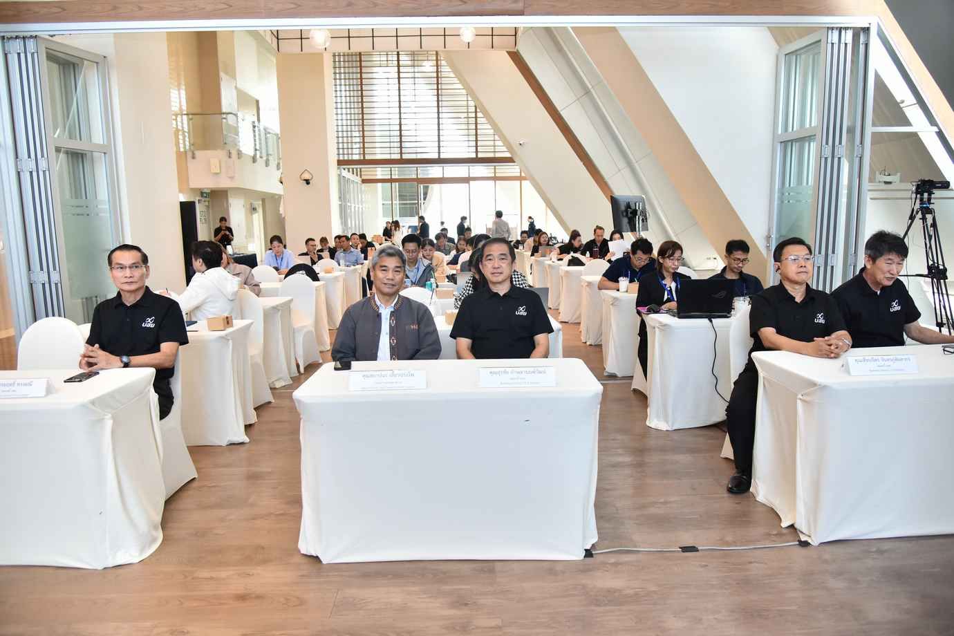Professionals seated at white-covered tables during a conference in a bright, modern event hall.