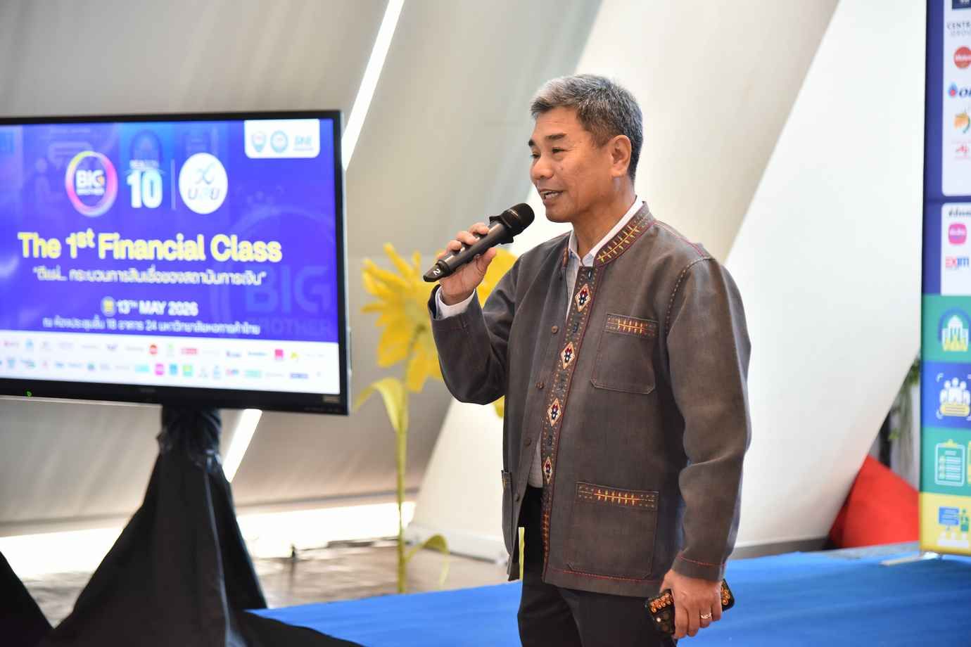 Man speaks into microphone on stage during 'The 1st Financial Class' event.