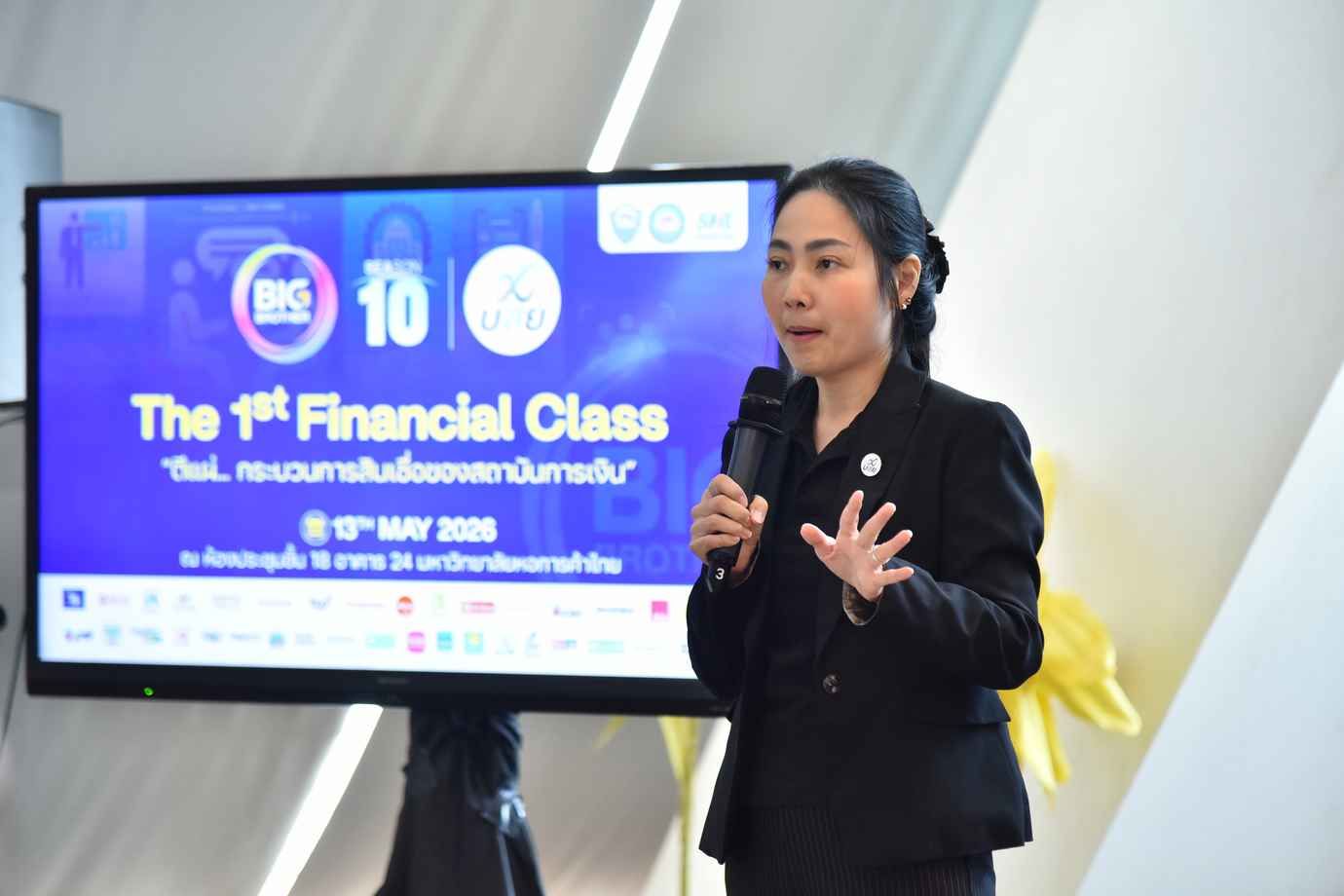 Woman in dark suit speaking into a microphone with 'The 1st Financial Class' on screen.