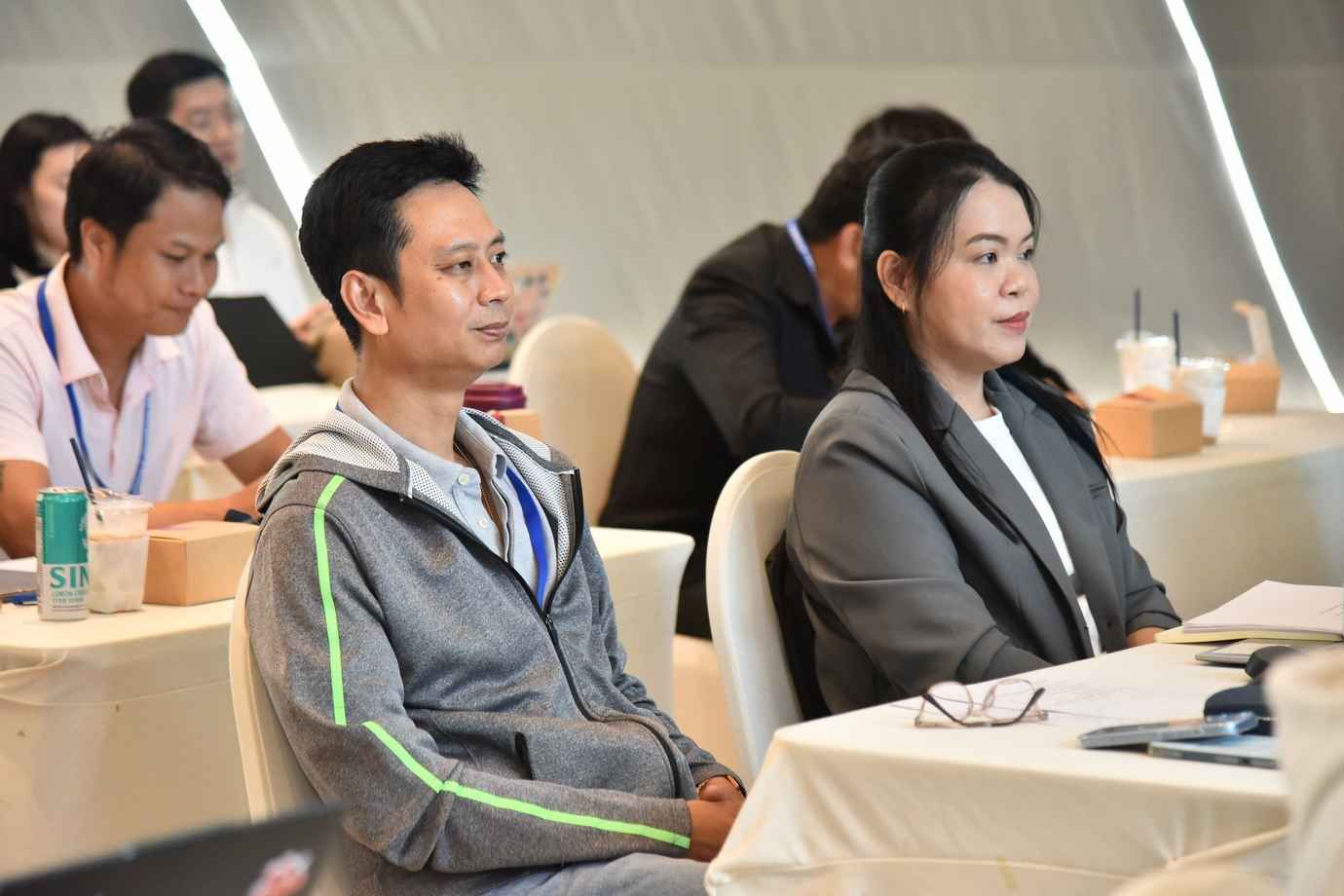 Two attendees, a man and a woman, watch attentively at a conference.