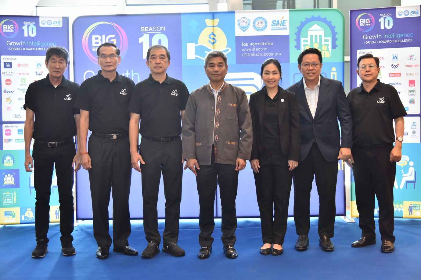 Seven professionals in black shirts stand before large branded event signs.