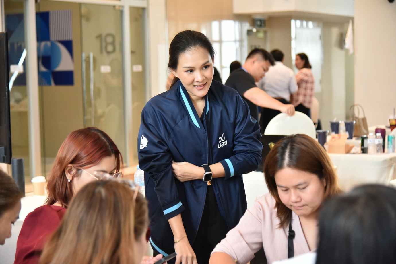 Smiling woman in a blue jacket standing over seated participants at an indoor event.