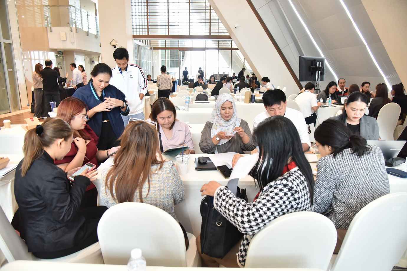 Diverse group of professionals collaborating at tables during a brightly lit conference or workshop.