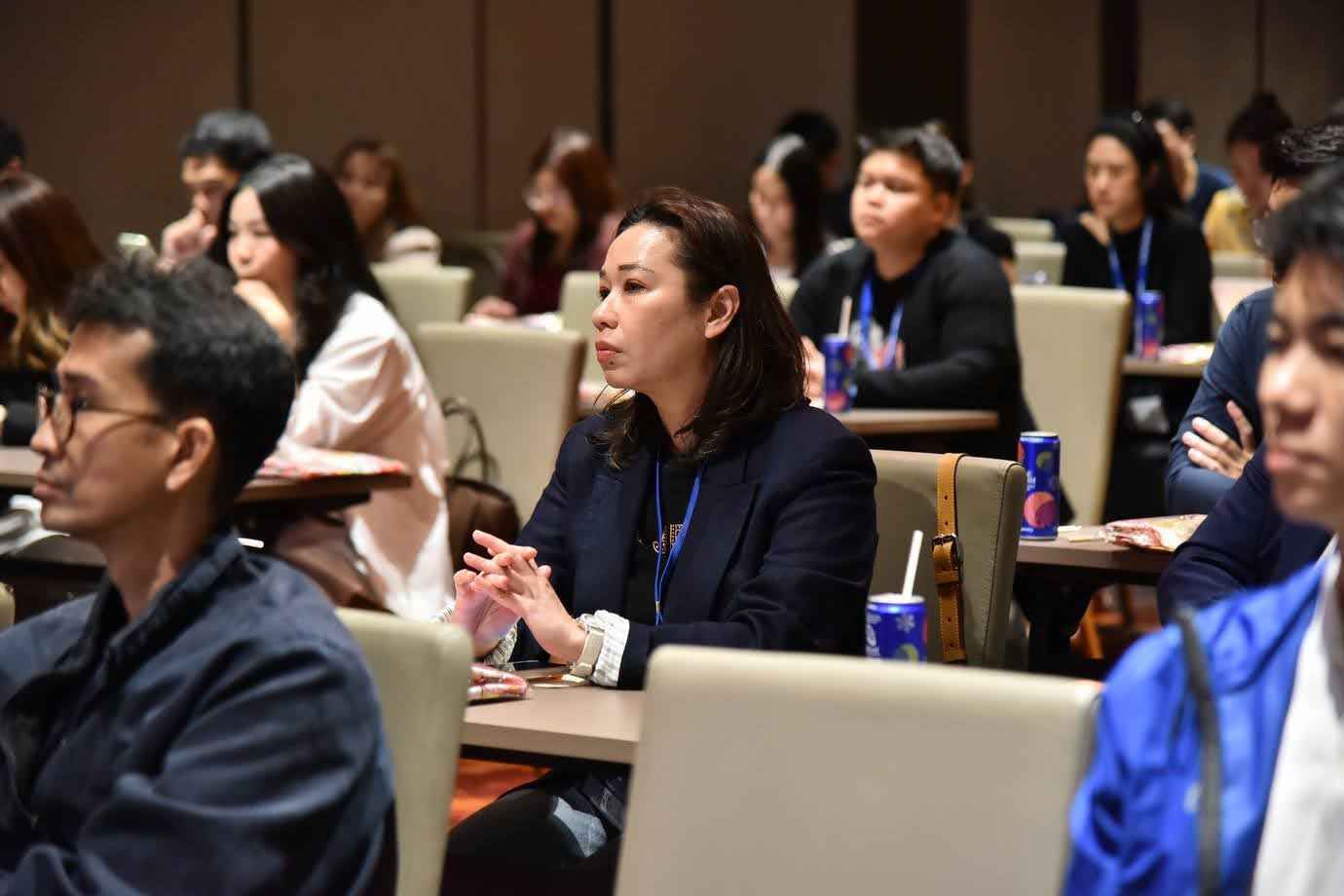 Woman in dark blazer attentively listening at a professional conference.