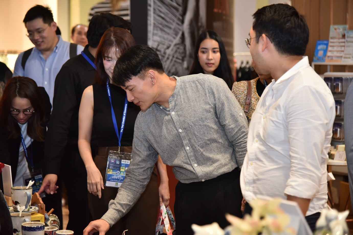 Man in grey shirt inspects items on a display table at an indoor event.