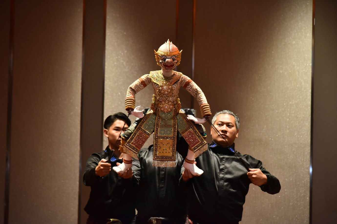 Two puppeteers skillfully operate a traditional Thai Hanuman puppet on a dark stage.