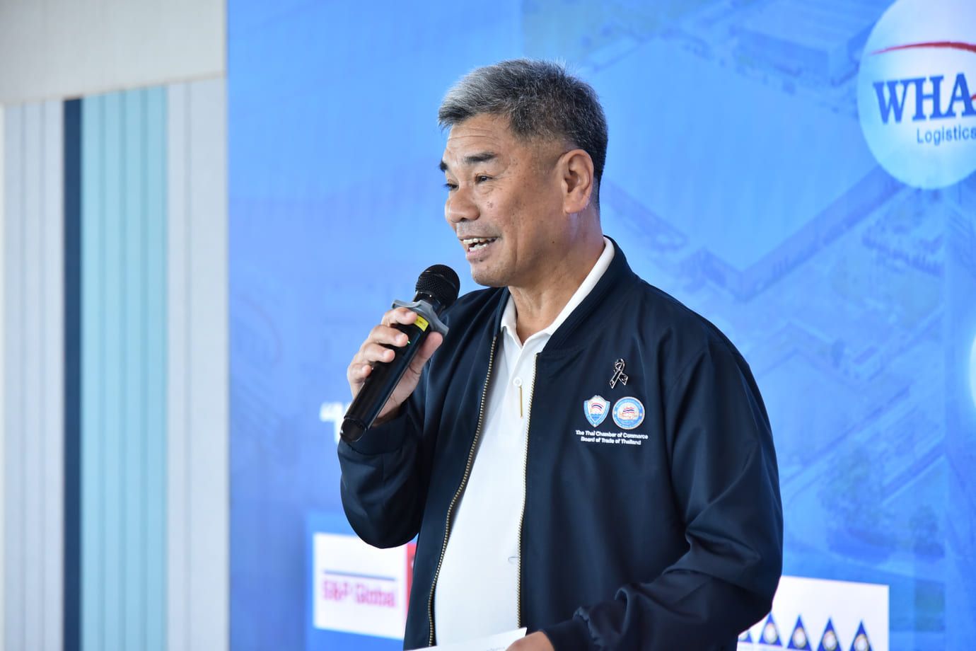 Asian man in blue jacket speaks into microphone at a professional event.