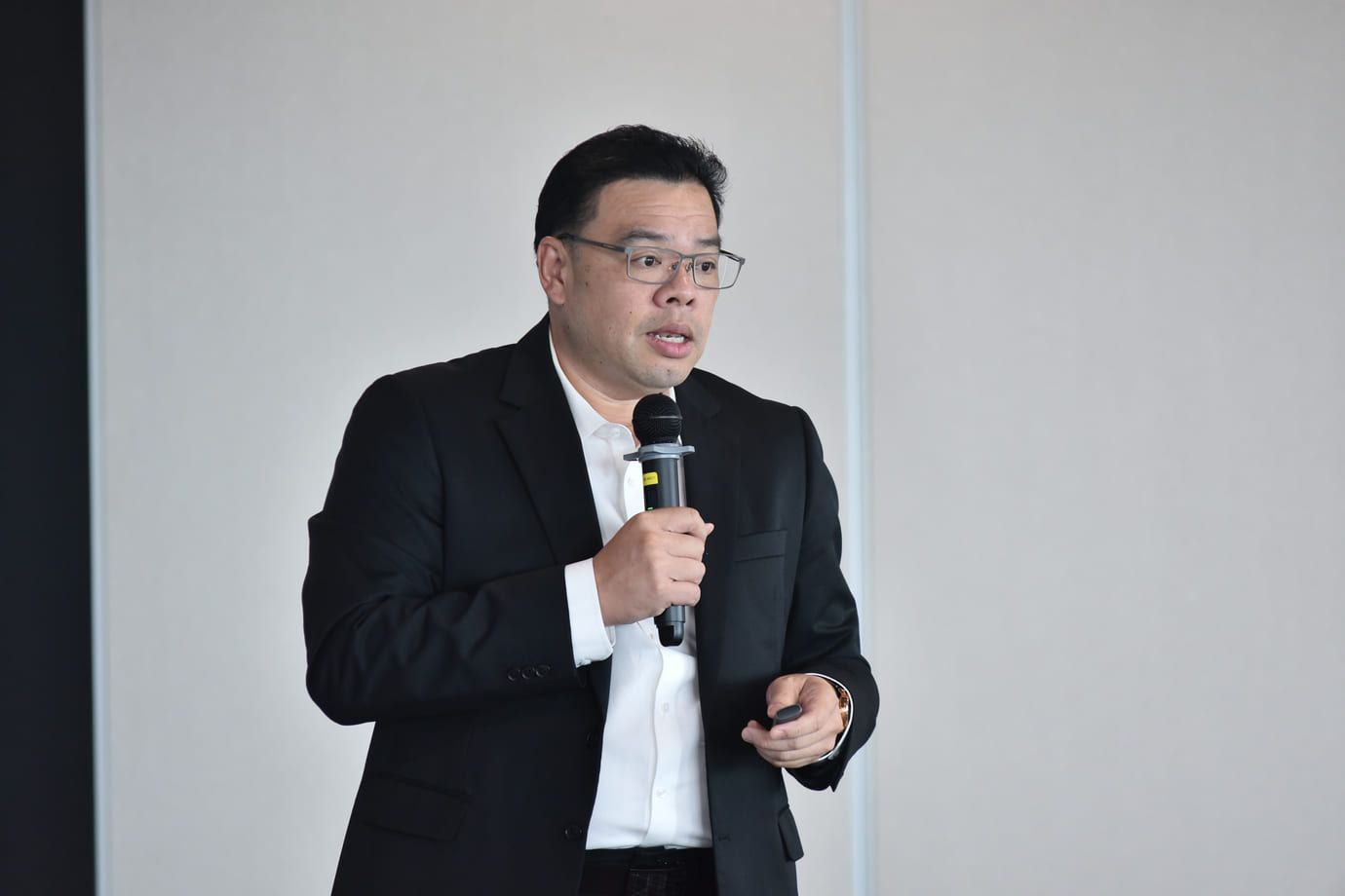 An Asian man in a black suit and white shirt speaks into a microphone.