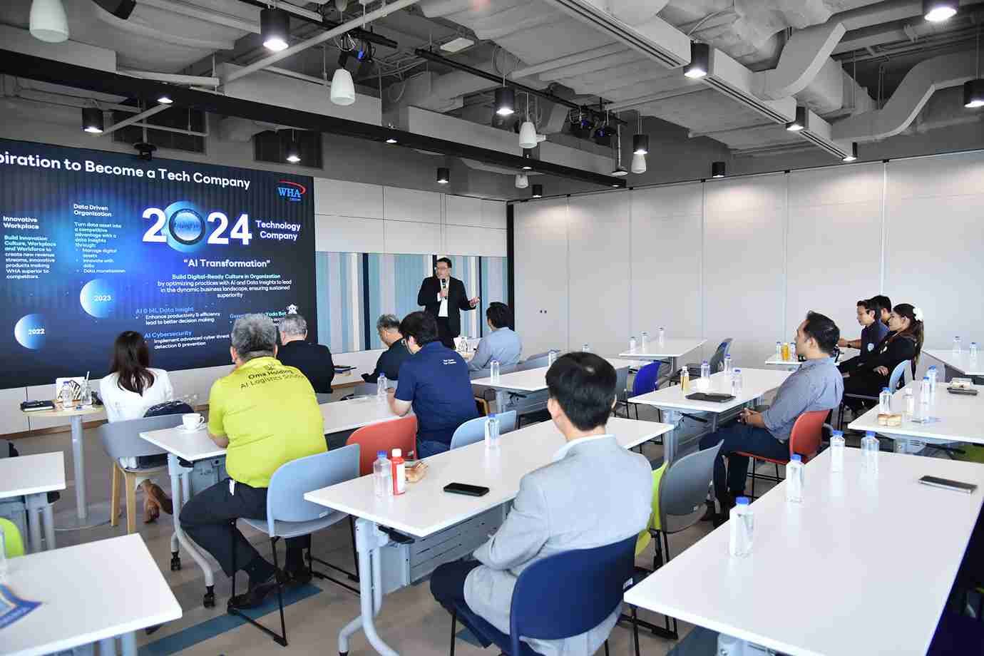 Attendees listen to a presenter in a modern conference room with a screen showing '2024 Tank Company'.